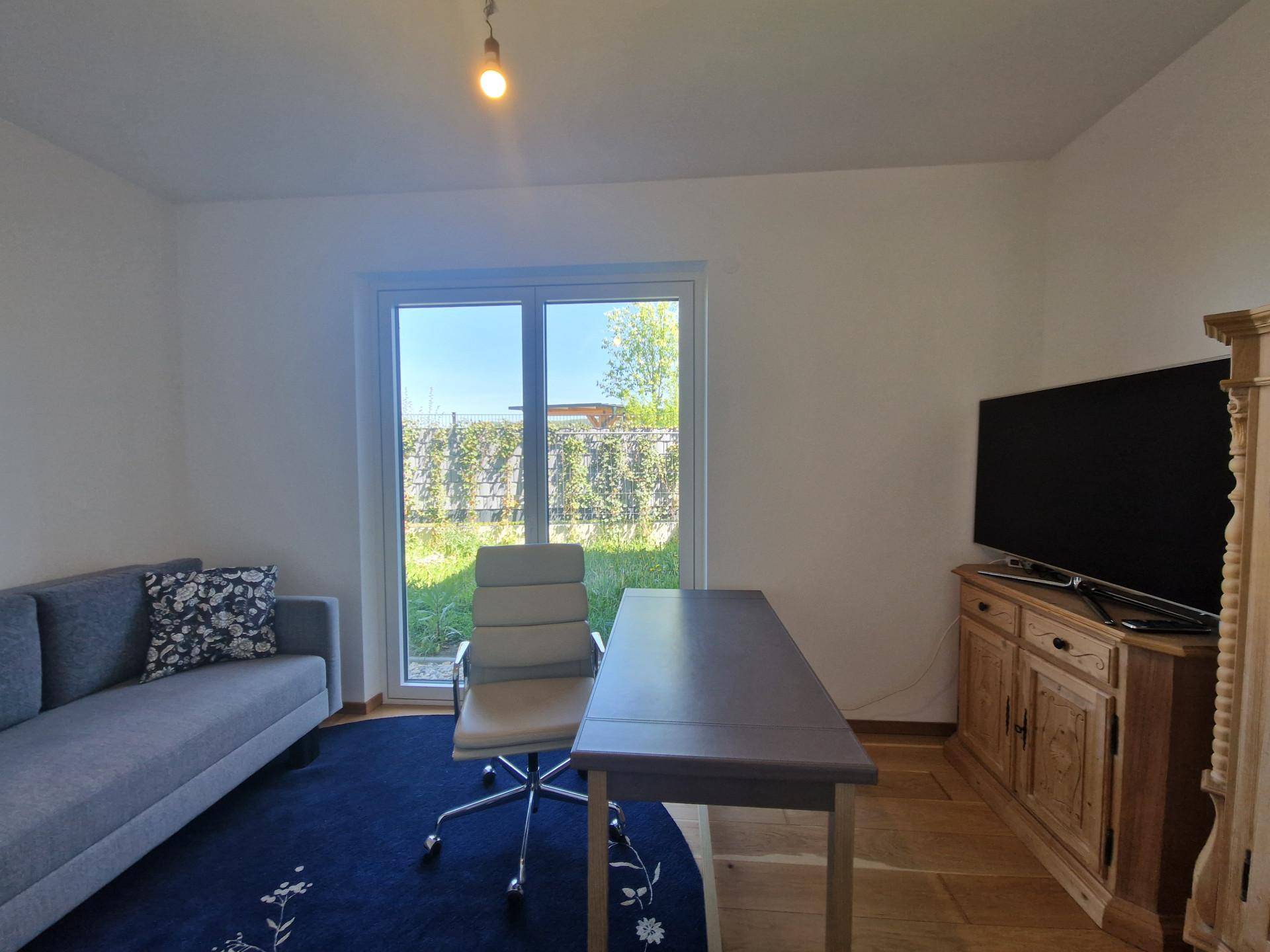 Helles Arbeitszimmer mit Holzboden, Schreibtisch und Sofa, bietet einen ruhigen Blick ins Grüne.