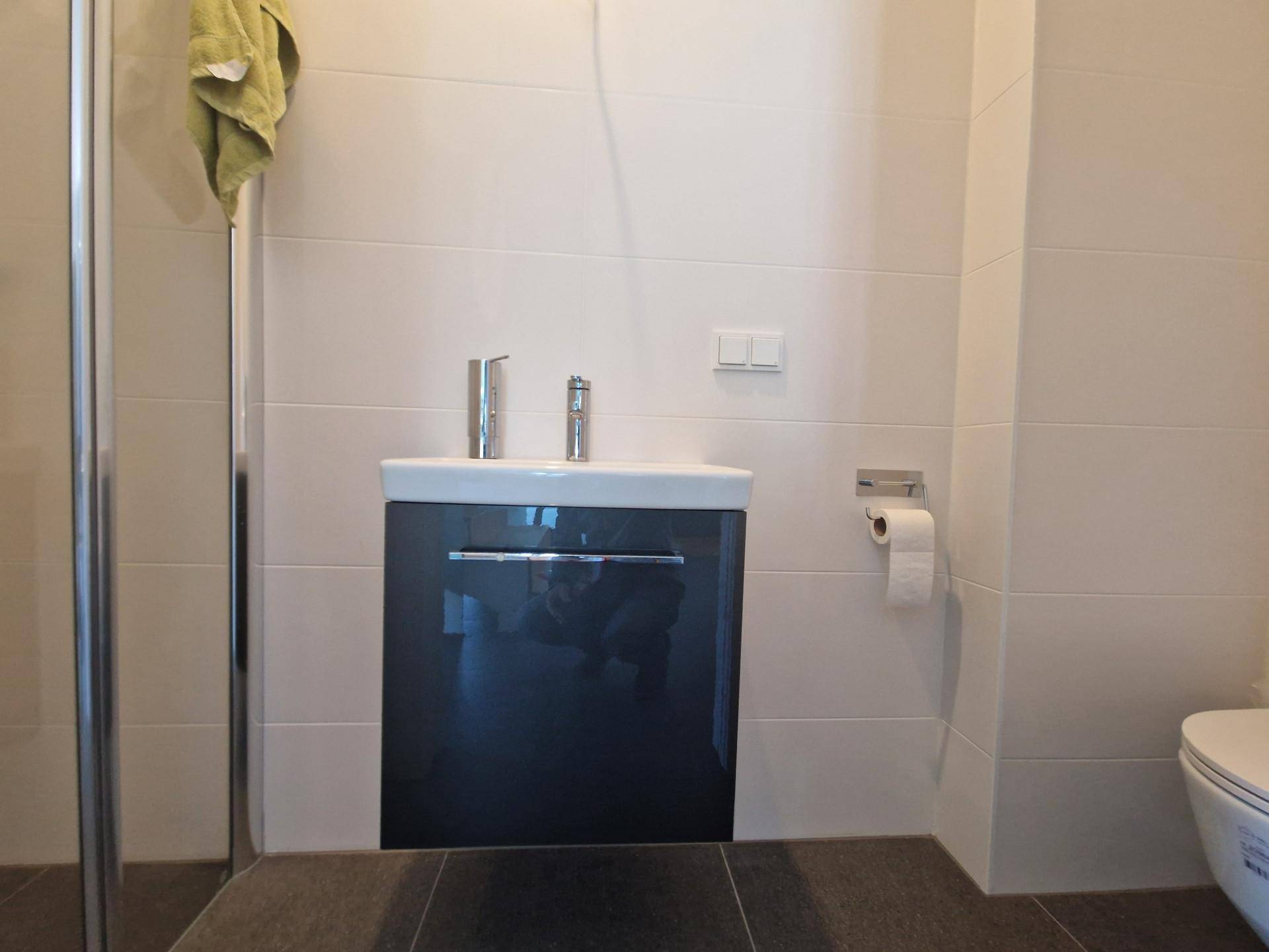 Modernes Badezimmer mit Waschtisch, wandhängendem WC und Duschkabine, hell gefliest.