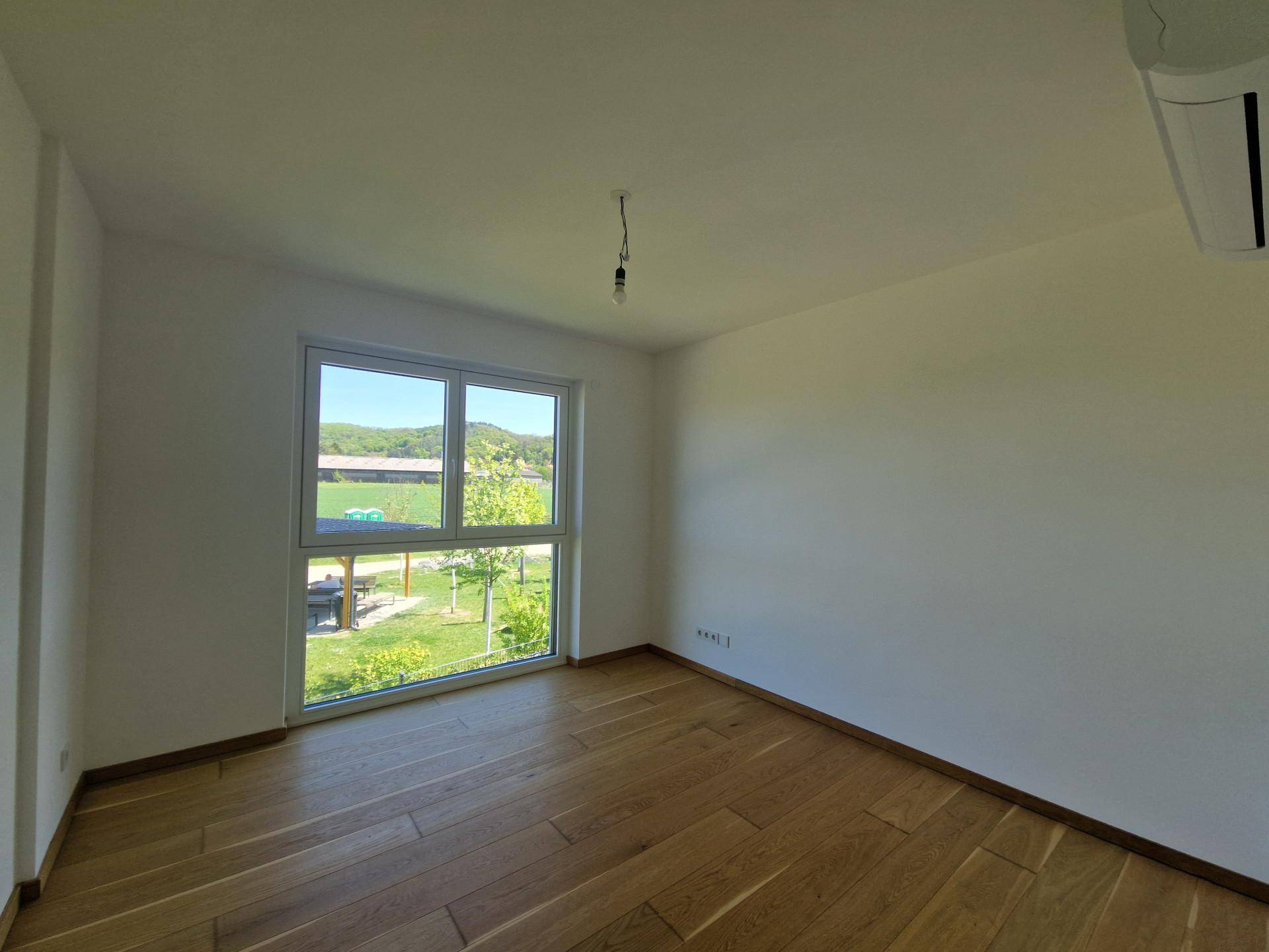 Helles Zimmer mit Holzboden und großem Fenster, das einen weiten Blick ins Grüne bietet.