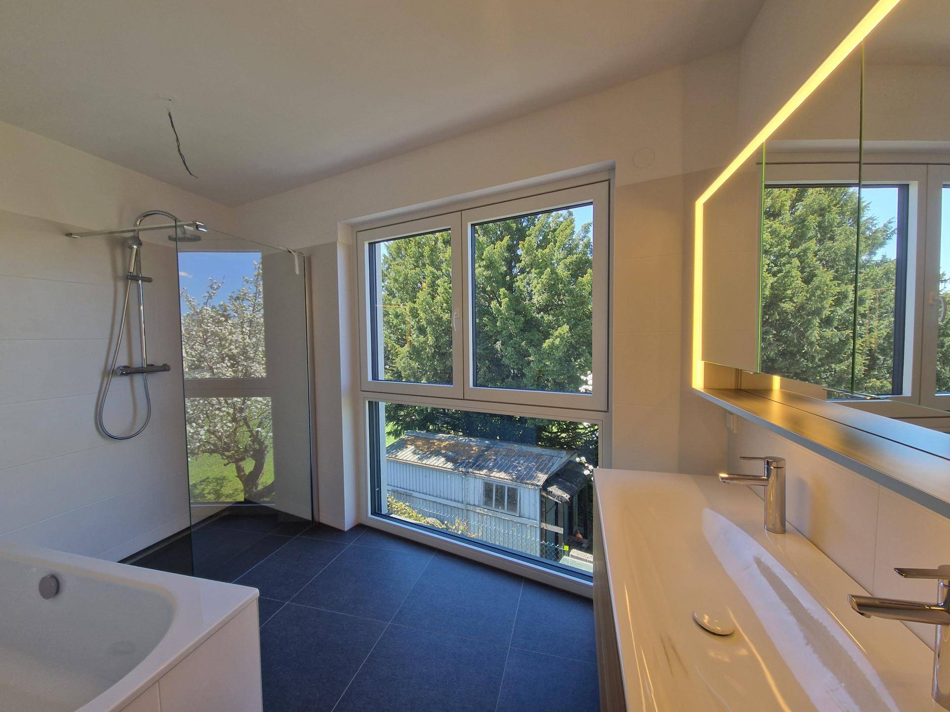 Modernes Badezimmer mit Doppelwaschbecken, Badewanne und Dusche, hell und mit Blick ins Grüne.