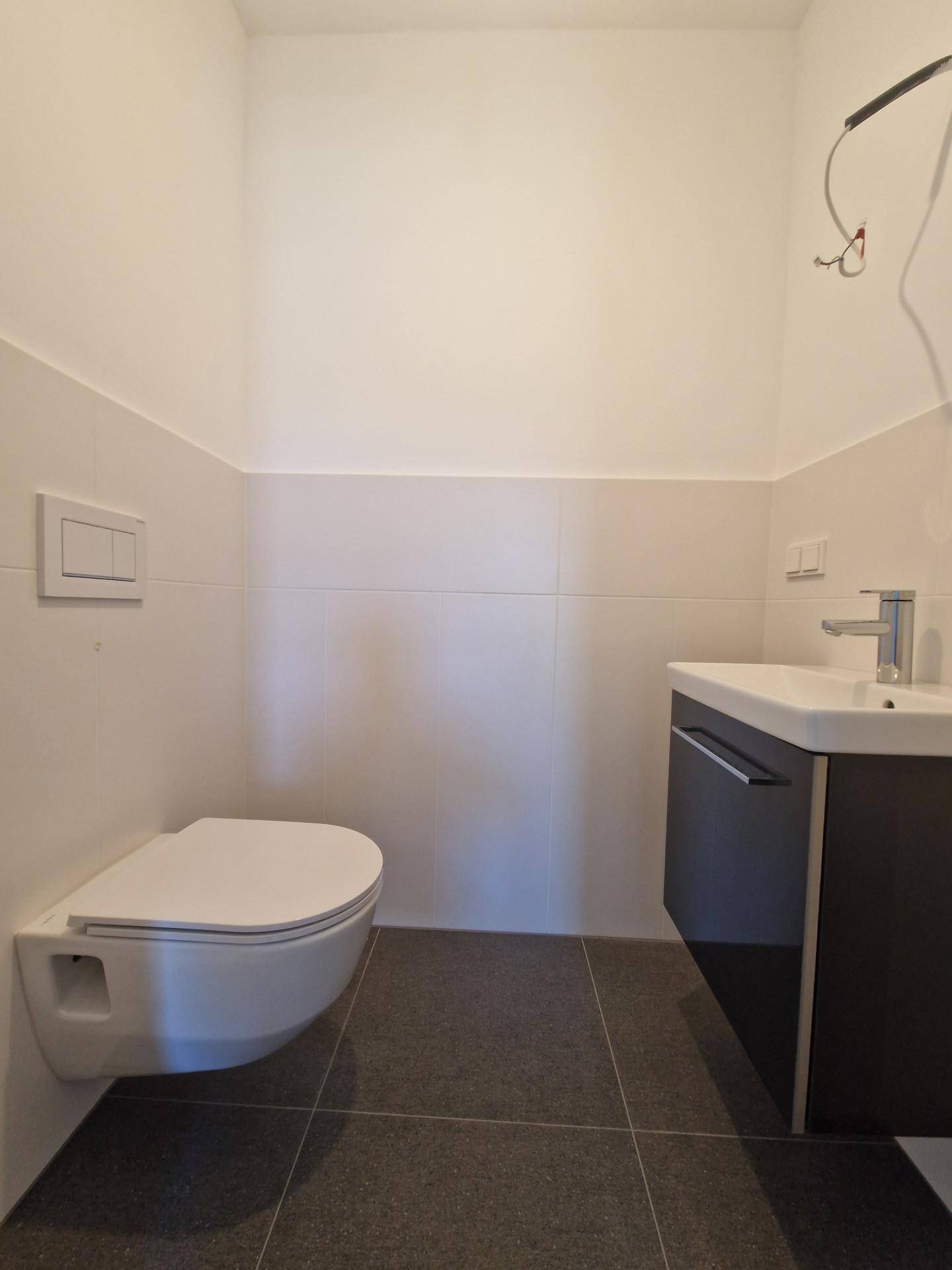 Modernes Gäste-WC mit wandhängendem WC und Waschtisch, in hellen und dunklen Fliesen gehalten.