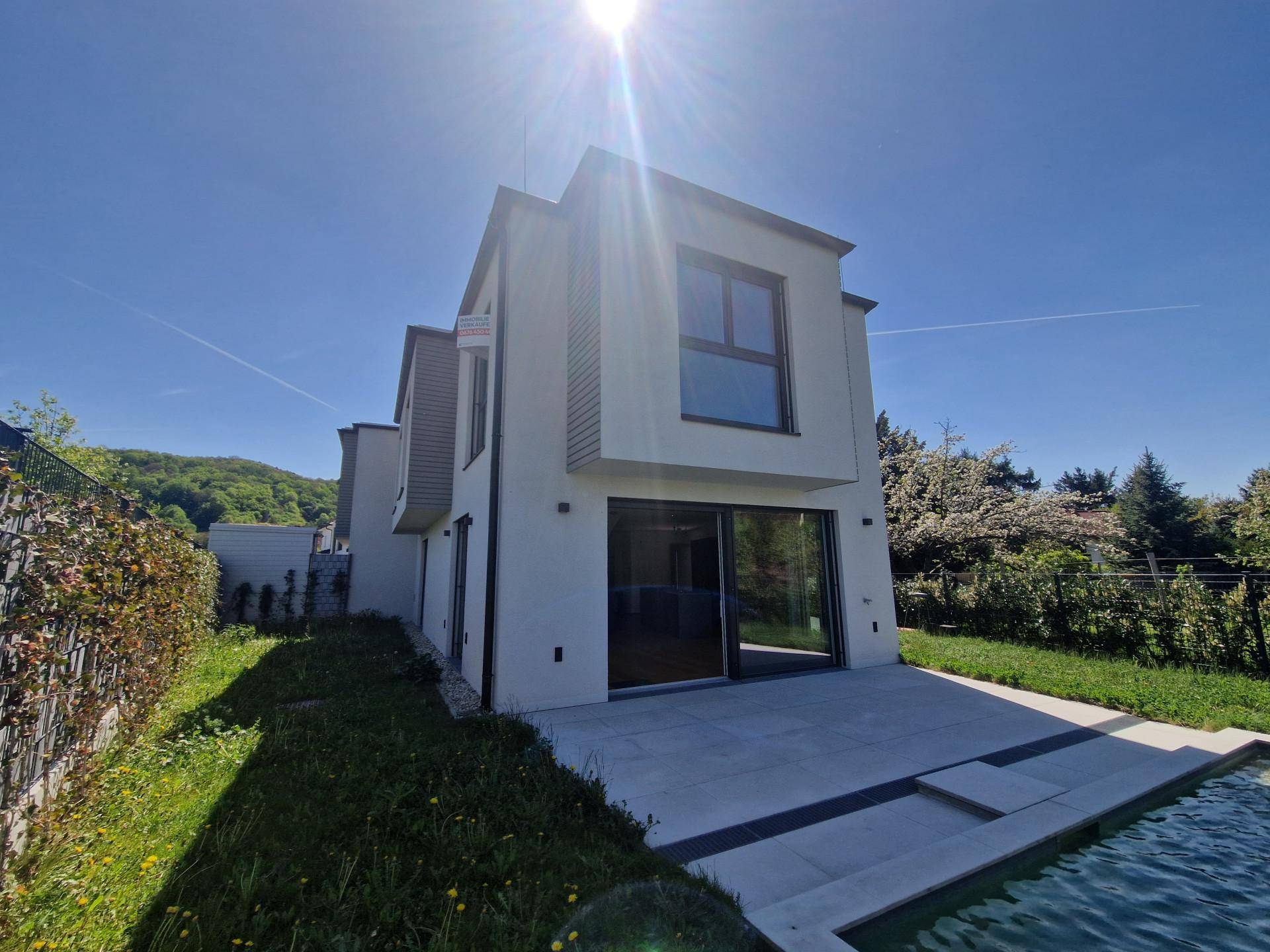 Moderne Hausfassade mit großen Glasfronten und einer Terrasse am Pool, unter strahlendem Sonnenschein.
