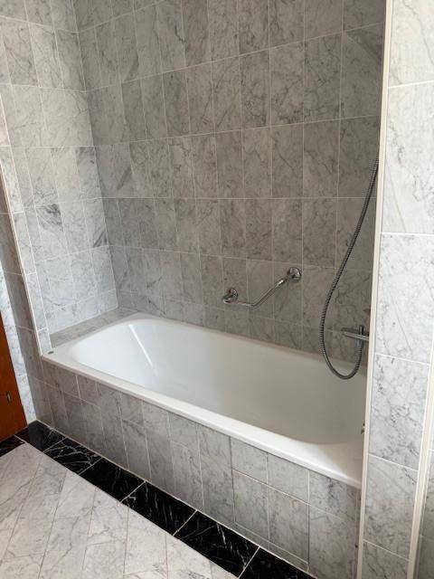 Badezimmer mit Badewanne und grauen Marmorfliesen an Wänden und Boden.