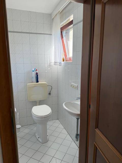 Separates WC mit weiß gefliesten Wänden, Toilette und kleinem Waschbecken.