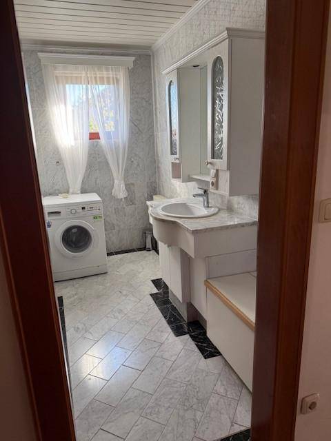 Geräumiges Badezimmer mit Marmorfliesen, Waschmaschine und Waschtisch mit Spiegelschrank.