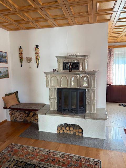 Wohnzimmer mit traditionellem Kachelofen, Holzboden und einer Sitzbank mit Holzablage.