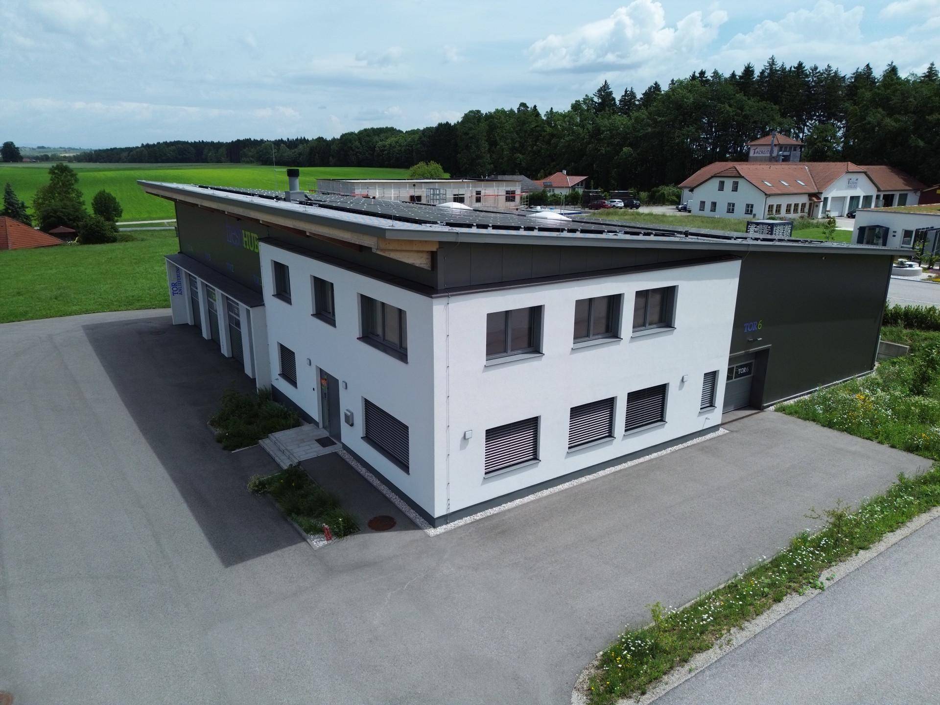 Modernes Gebäude mit weißer und dunkelgrauer Fassade, umgeben von grünen Feldern und einem Parkplatz.