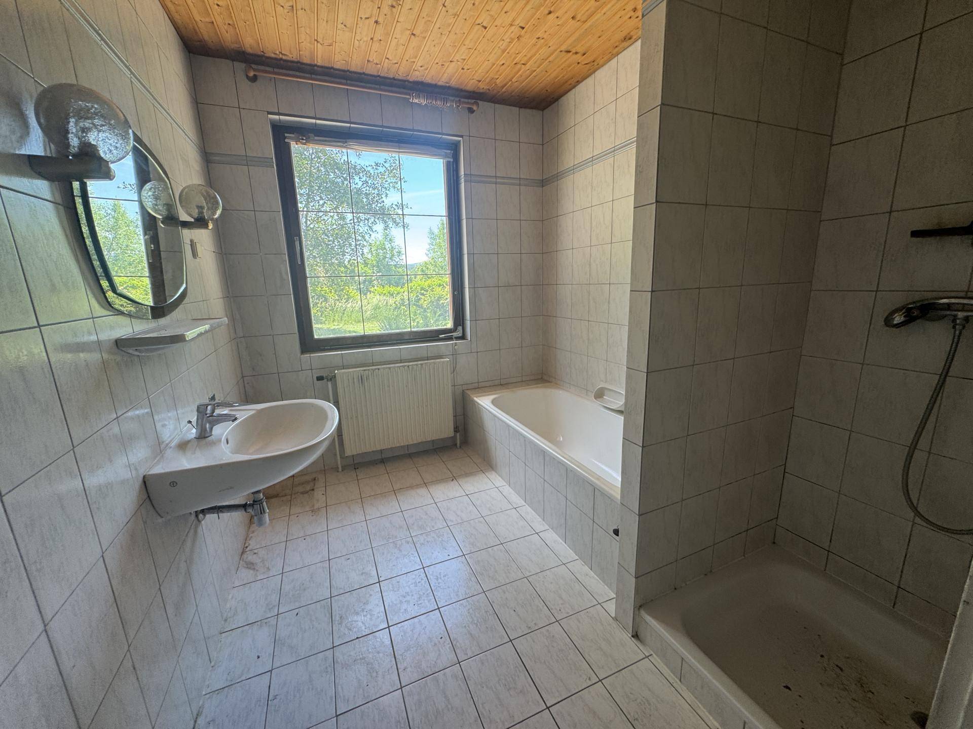 Badezimmer mit weißen Fliesen, Badewanne, Duschbereich, Waschbecken und einem Fenster.