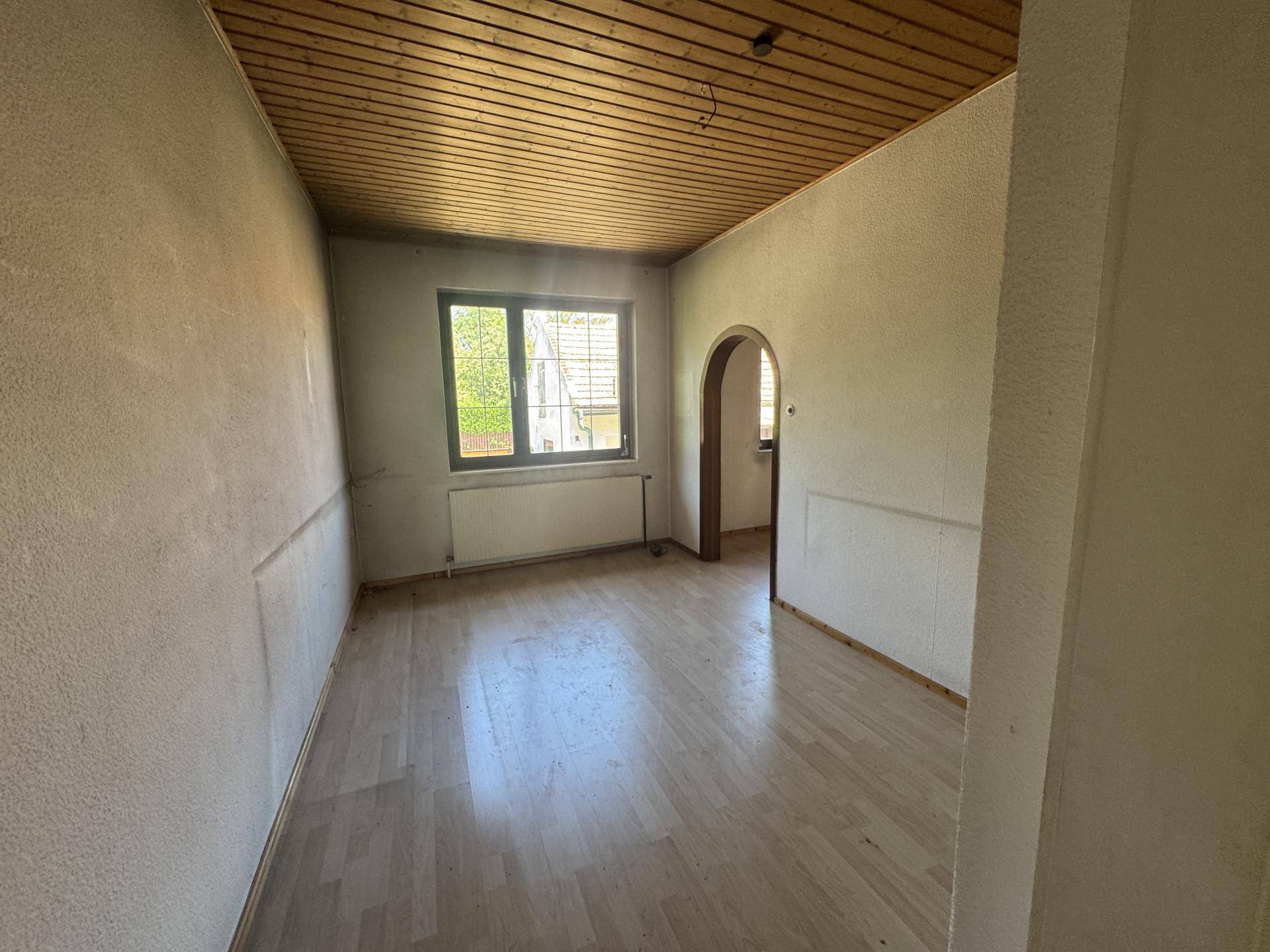 Leeres Zimmer mit Parkettboden, Holzdecke und einem Fenster, das viel Licht hereinlässt.