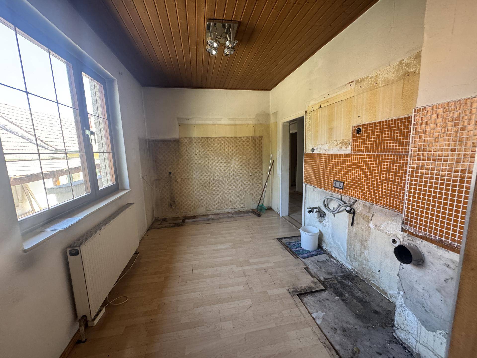 Küche in Renovierung mit freigelegten Wänden, alten Fliesen und einer Holzdecke.