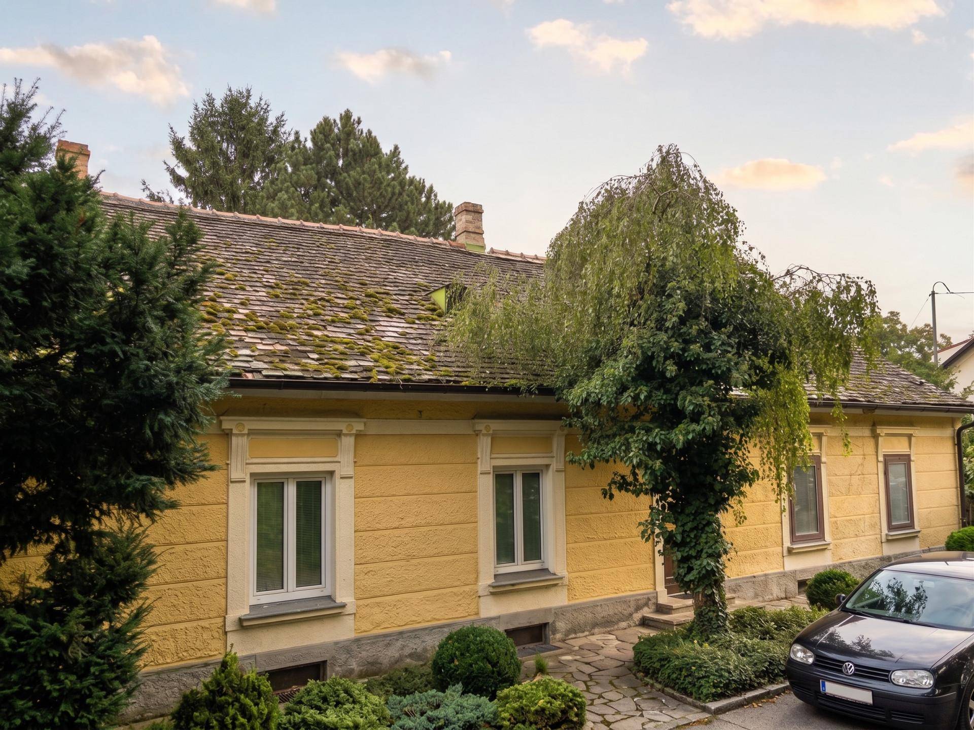 Altes, gelbes Haus mit traditioneller Architektur, moosbewachsenem Dach und gepflegtem Vorgarten.