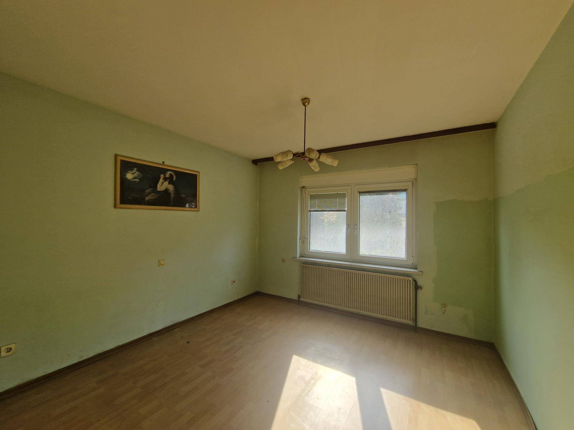 Leeres Schlafzimmer mit hellgrünen Wänden, Holzfußboden und Fenster.