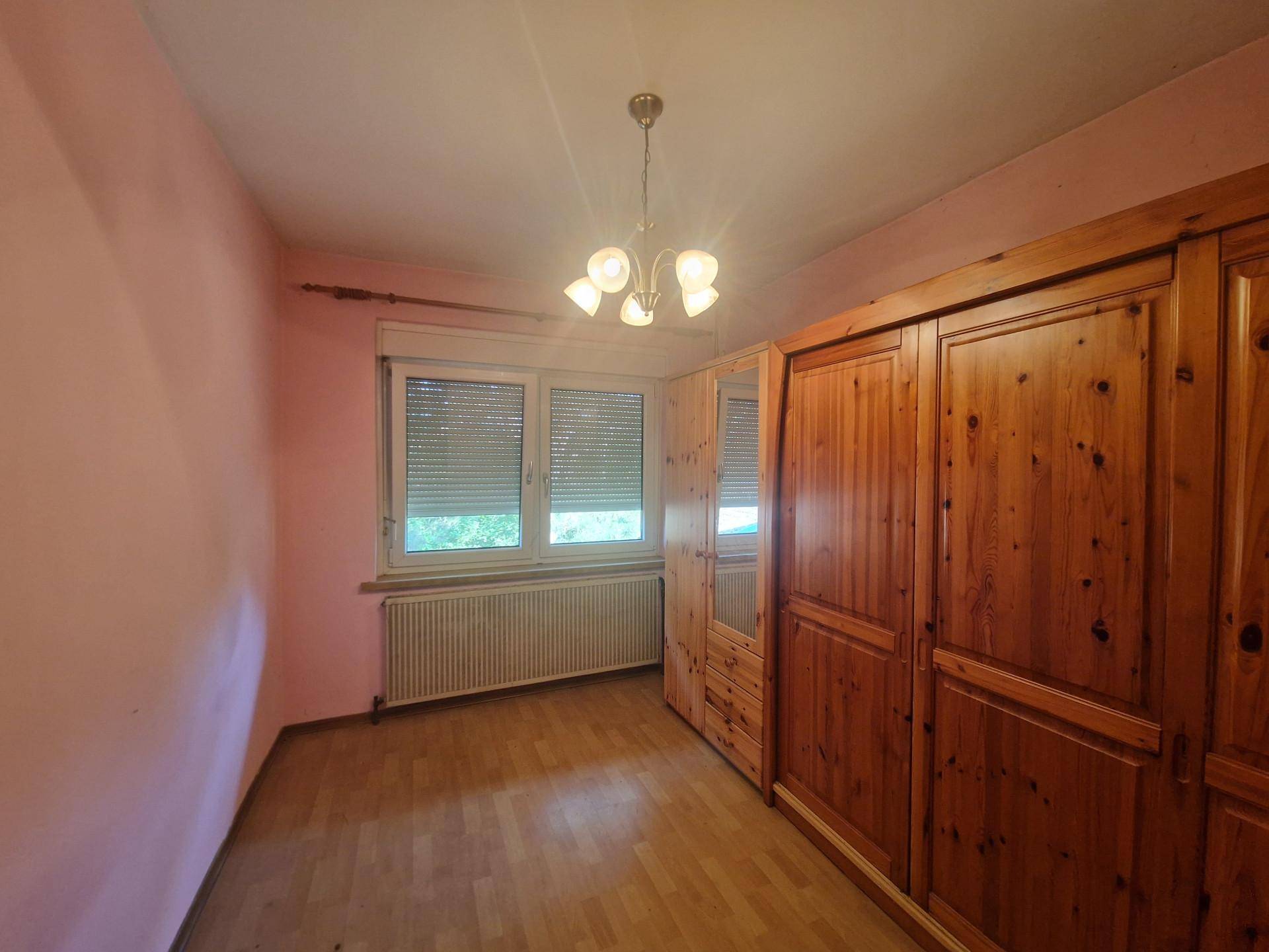 Schlafzimmer mit großem Holzschrank, rosa Wänden und Laminatboden.