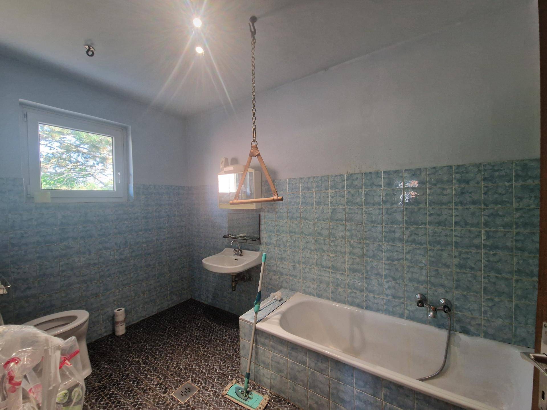 Badezimmer mit Badewanne, Waschbecken, WC und blauen Fliesen.