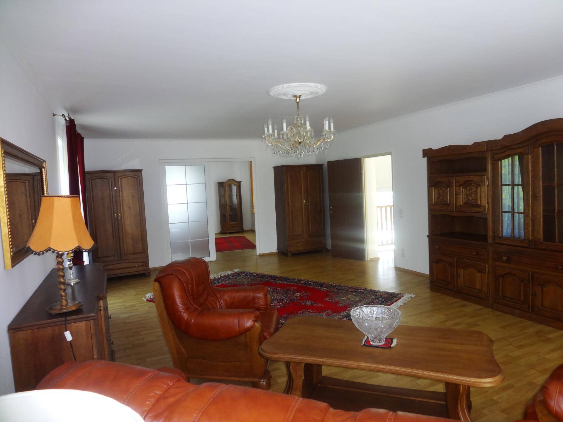 Geräumiges Wohnzimmer mit traditionellen Holzmöbeln, Ledersofa und Kronleuchter.