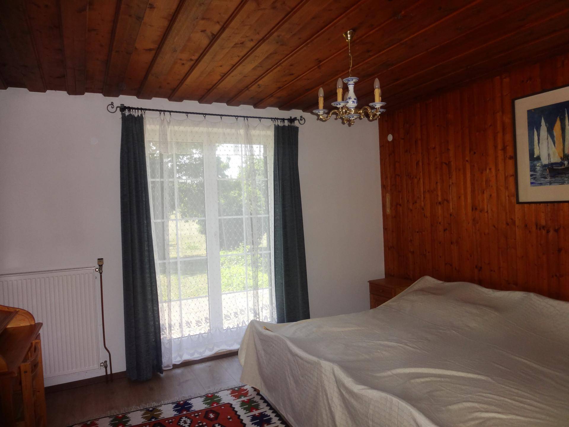 Schlafzimmer mit Holzdecke, Holzvertäfelung und Zugang zu einem Fenster mit Blick ins Grüne.