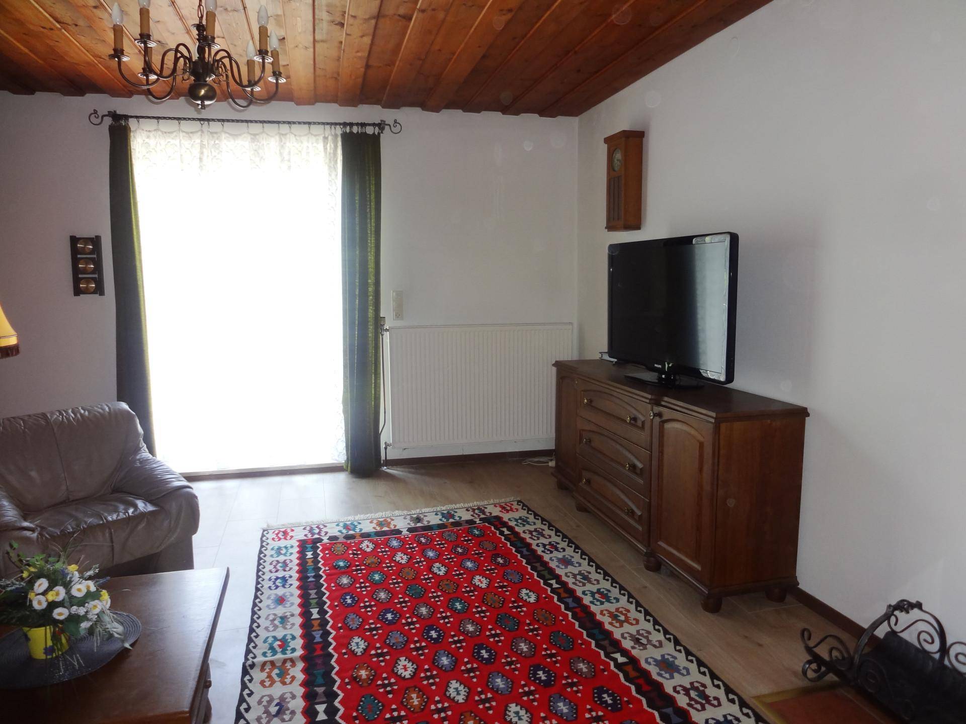 Wohnbereich mit Holzdecke, traditionellem Teppich und einem Fernseher auf einem Holzschrank.