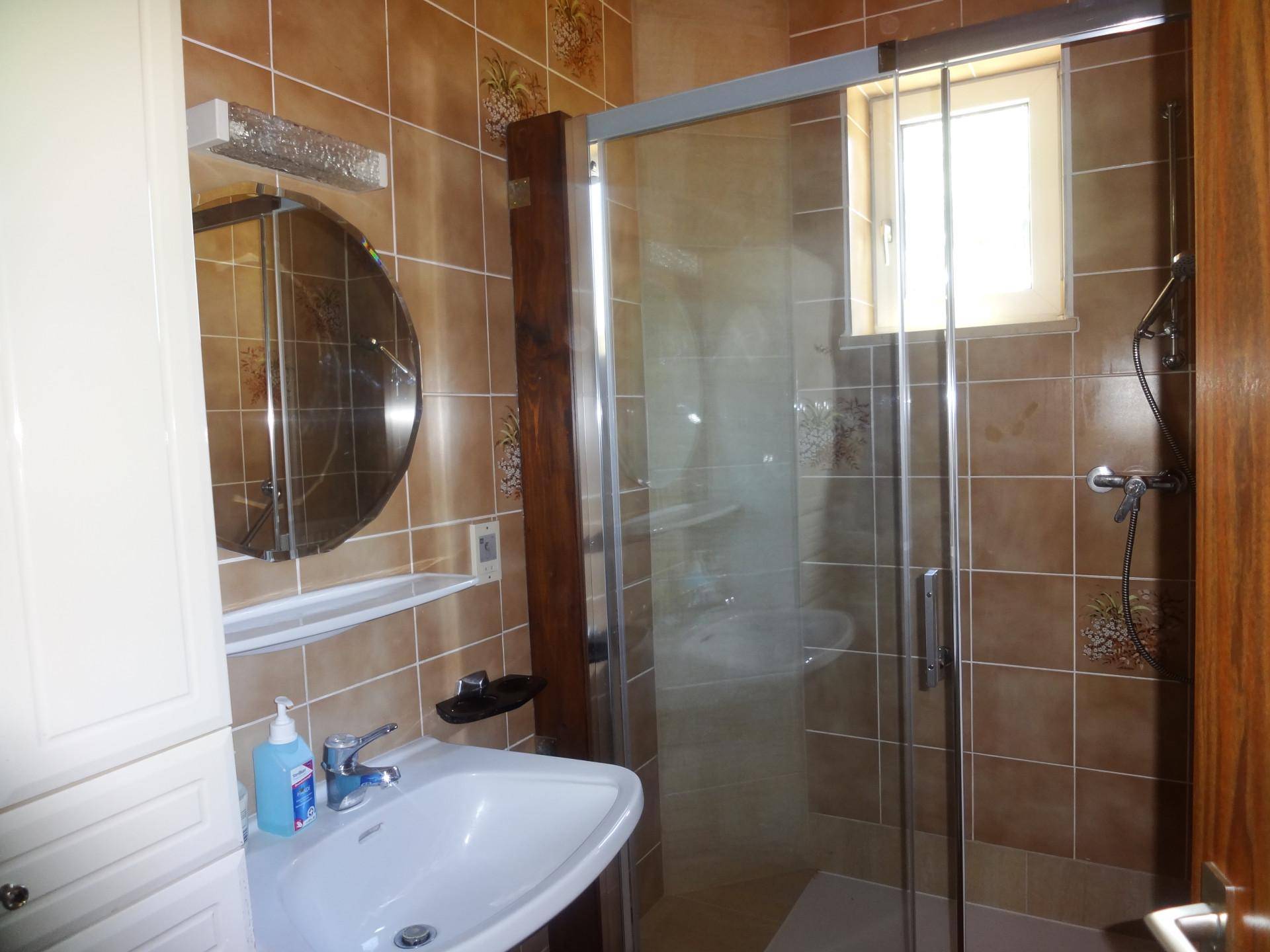 Funktionales Badezimmer mit braunen Fliesen, Duschkabine, Waschbecken, Spiegel und einem Fenster für Tageslicht.
