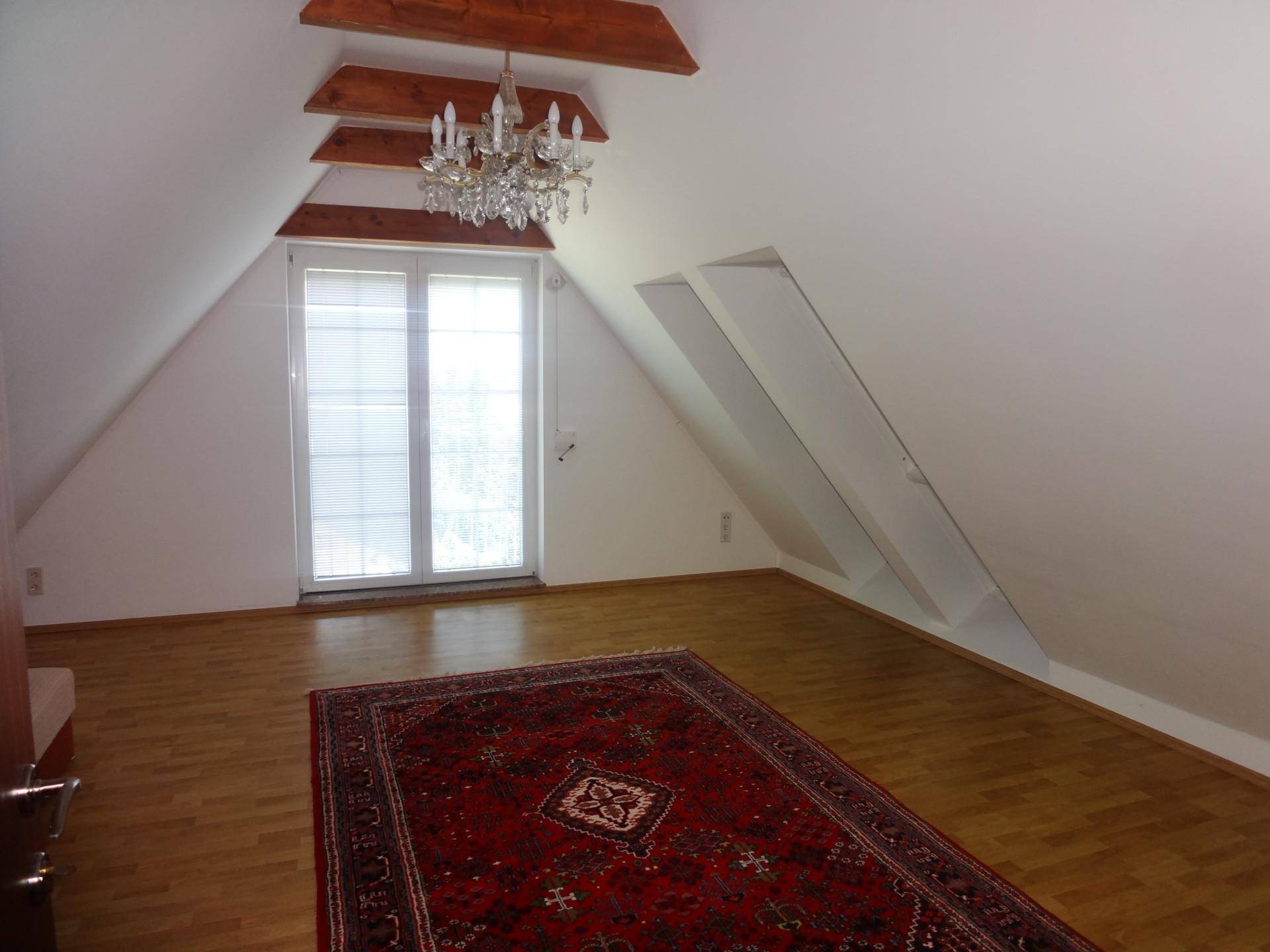 Geräumiges Dachzimmer mit Holzbalken, Dachfenster und Teppichboden.