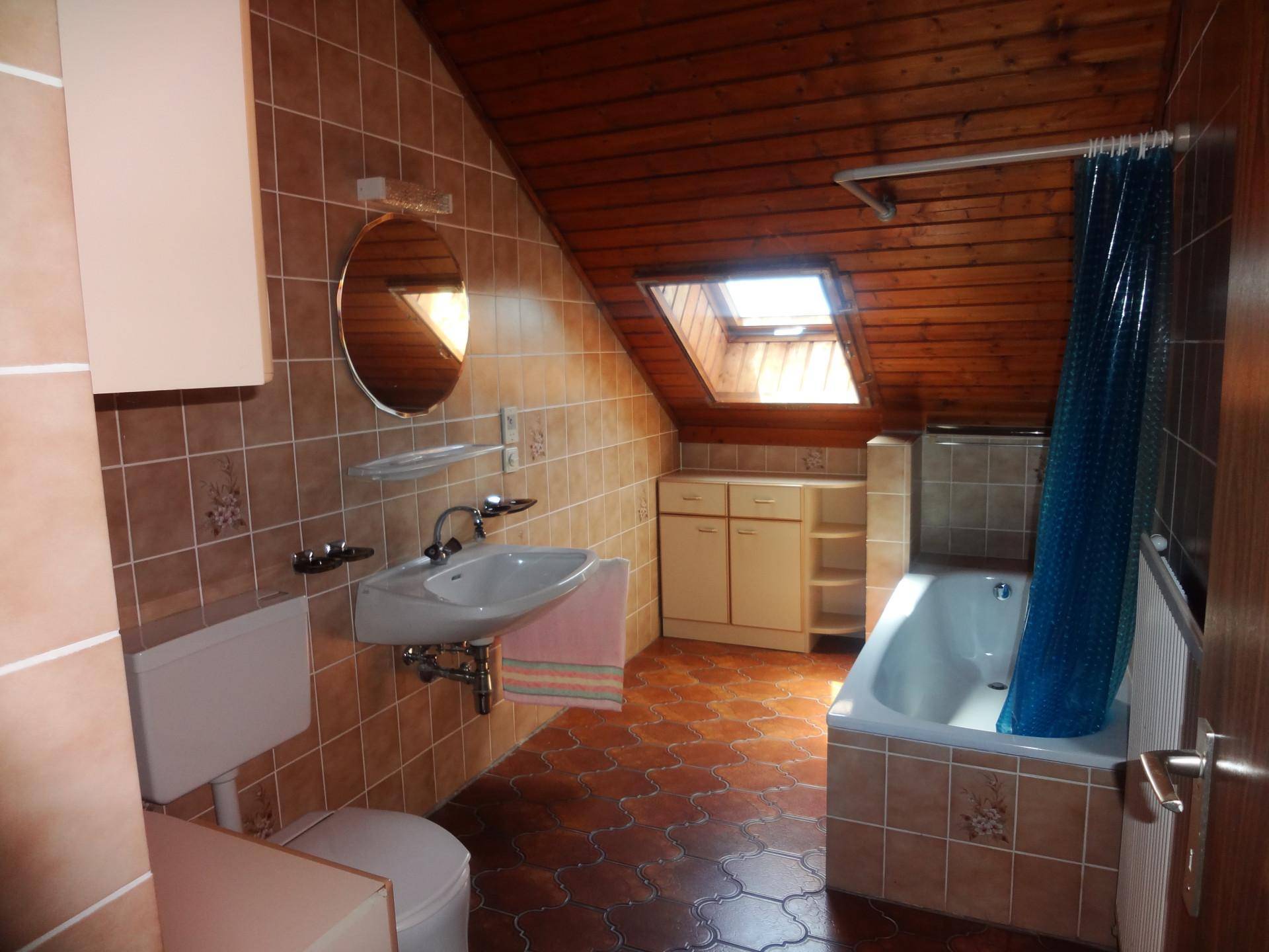 Badezimmer im Dachgeschoss mit Badewanne, Dachfenster und Terrakotta-Fliesen.