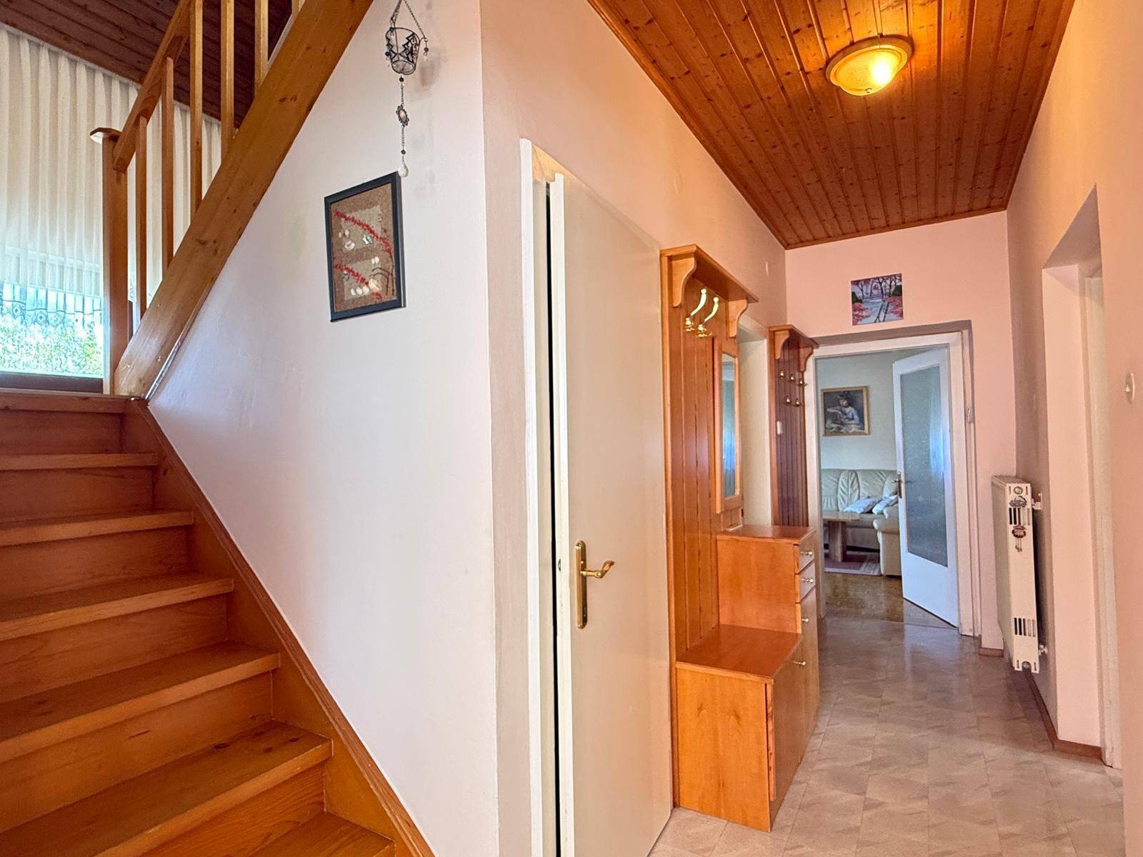 Flur mit Holztreppe, Garderobe und holzgetäfelter Decke, der zu den oberen Etagen führt.