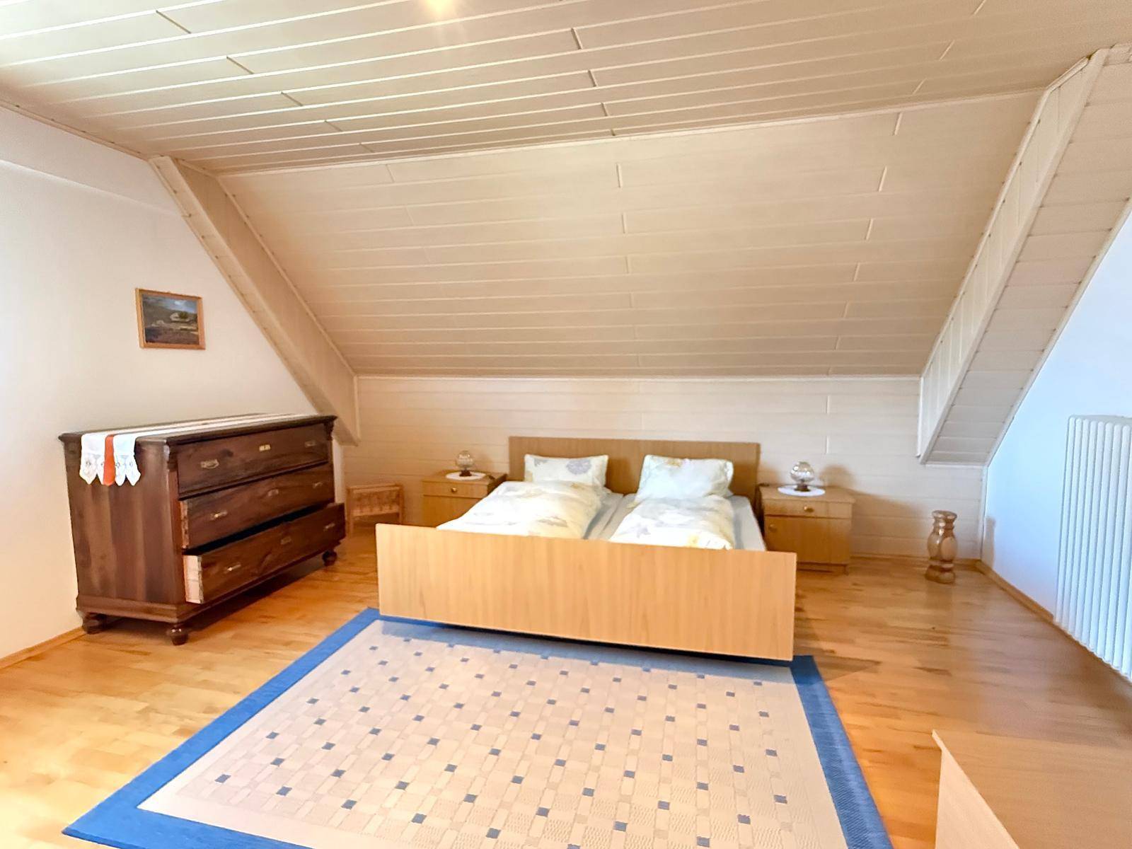 Gemütliches Schlafzimmer im Dachgeschoss mit Holzboden, Doppelbett und schrägen Wänden.