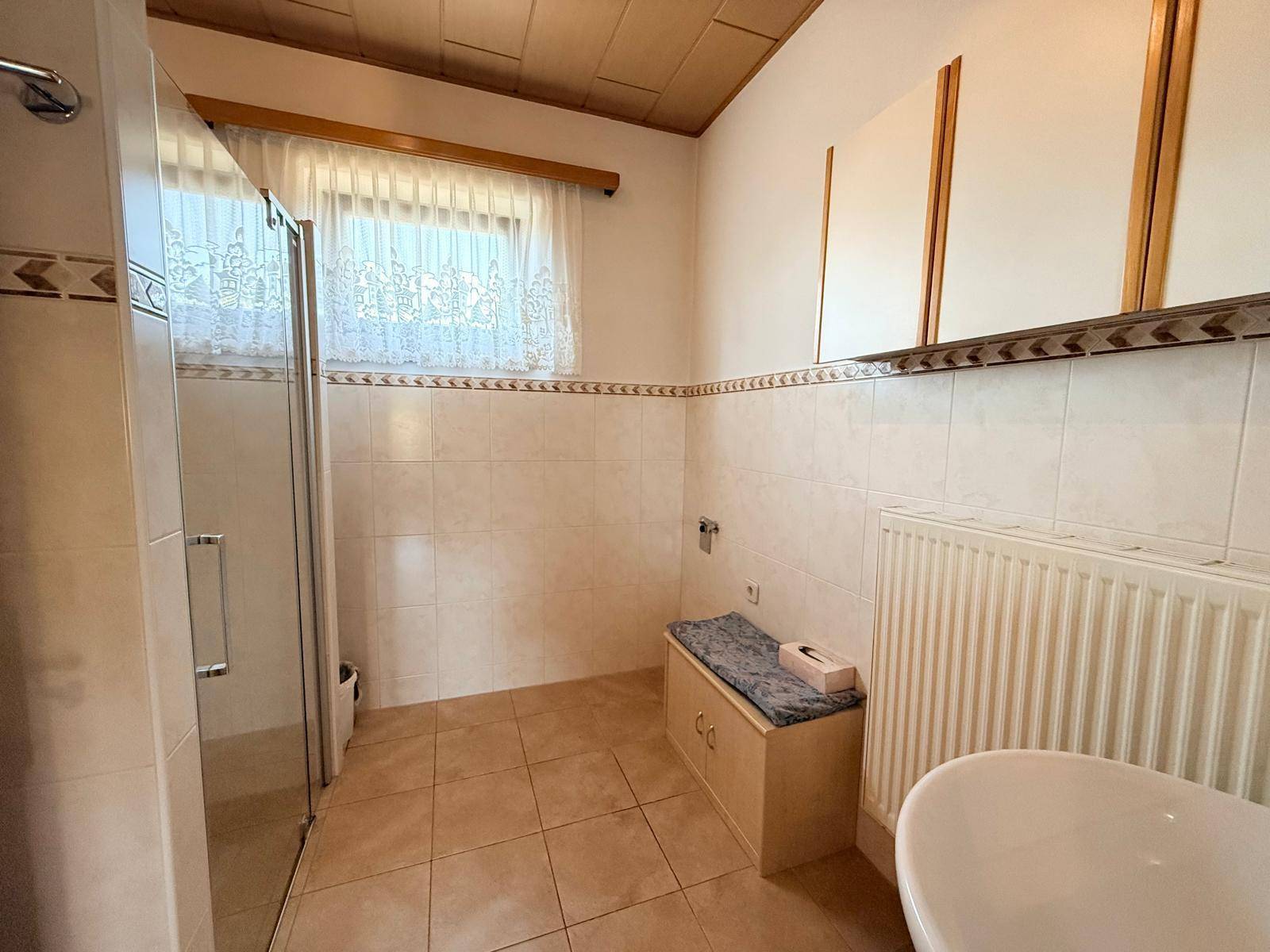 Badezimmer mit Duschkabine, Fliesenboden und einem Fenster, das für natürliches Licht sorgt.