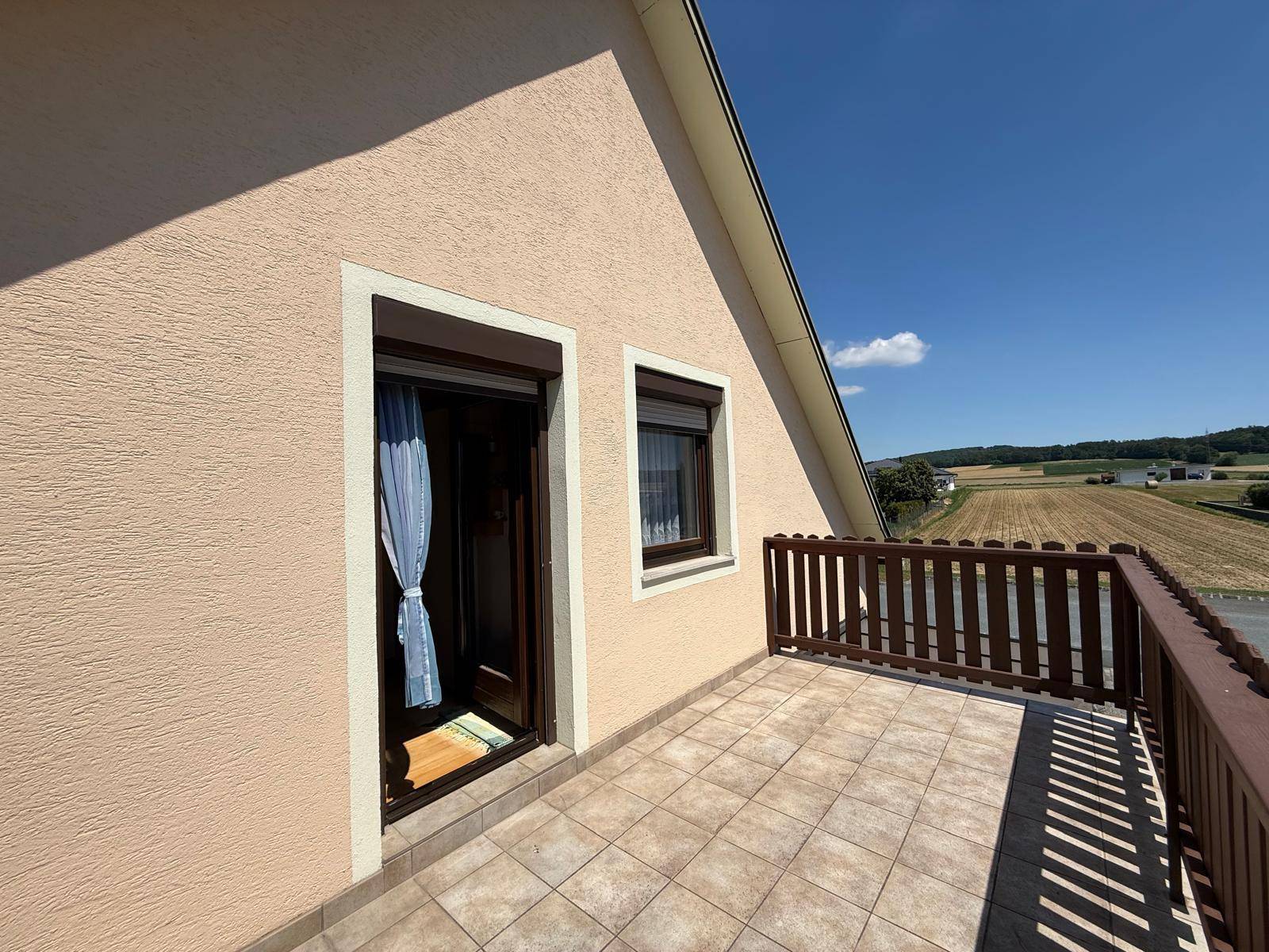 Kleiner Balkon mit Fliesenboden und Holzgeländer, der einen weiten Blick in die Landschaft bietet.