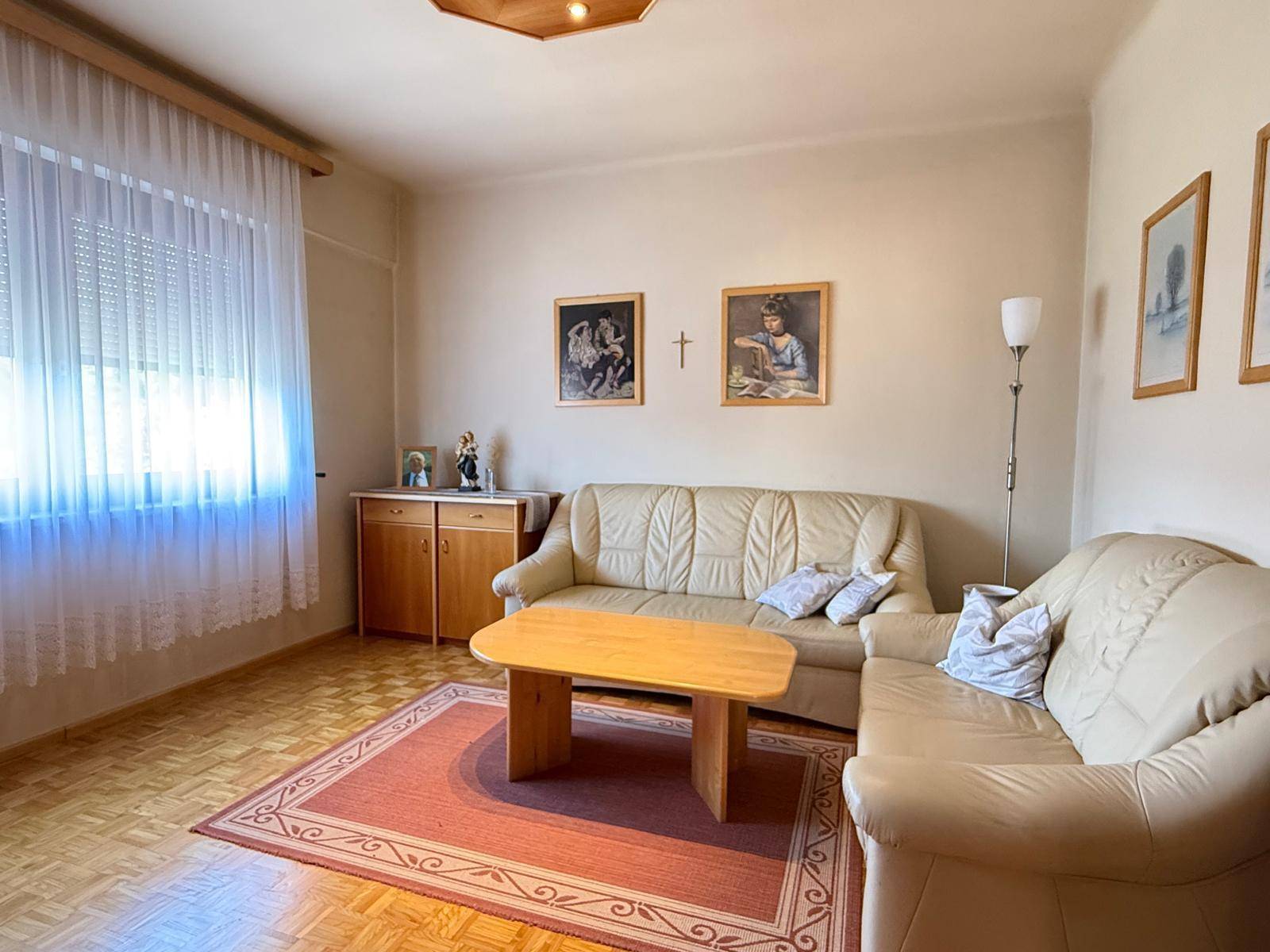 Helles Wohnzimmer mit beigen Ledersofas, Holztisch und Parkettboden, dekoriert mit Bildern.