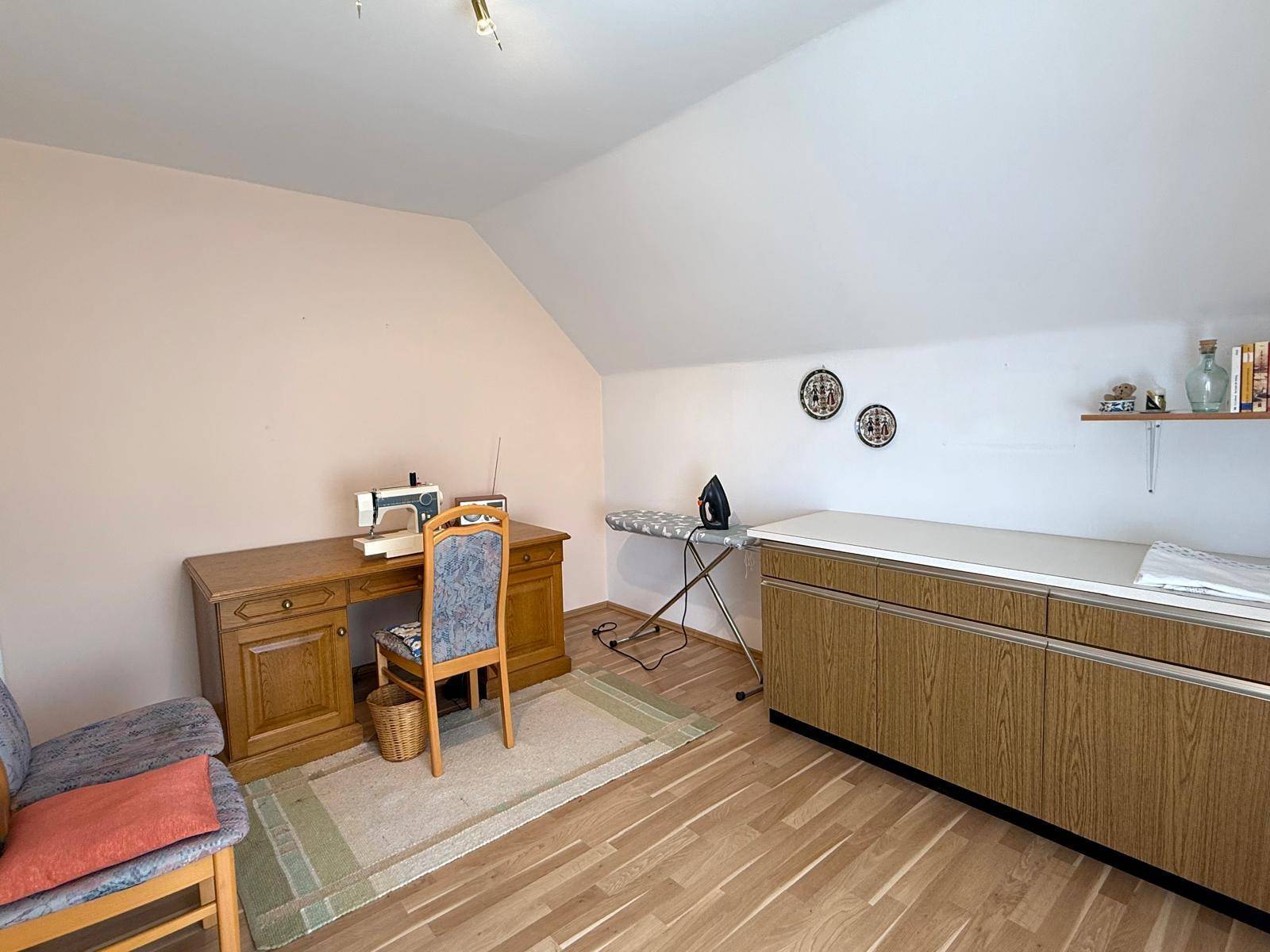 Dachgeschossraum als Arbeitszimmer mit Schreibtisch, Bürostuhl und Holzboden unter schrägen Wänden.