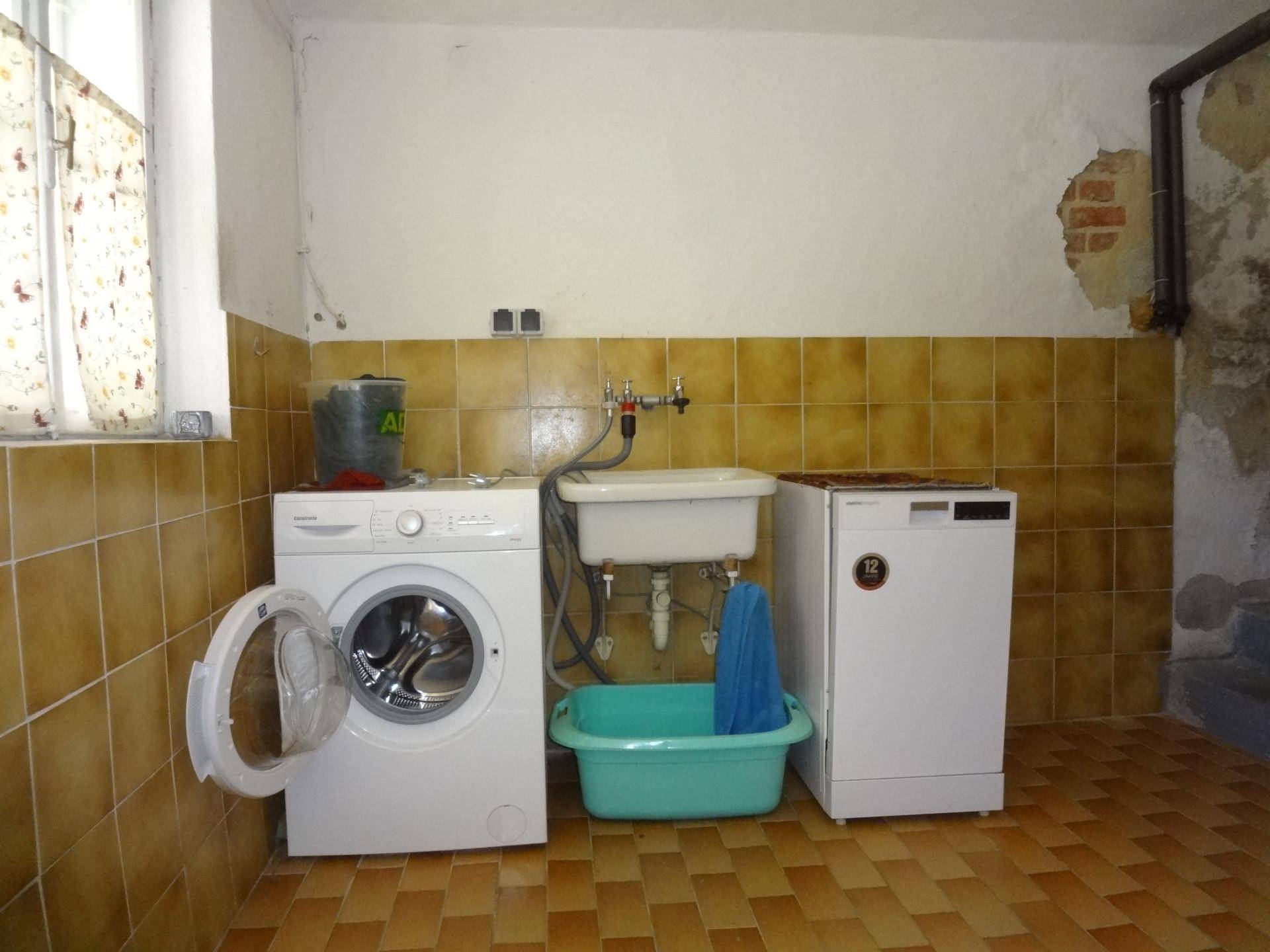 Waschküche mit Waschmaschine, Spülbecken und braunen Wandfliesen in funktionalem Zustand.