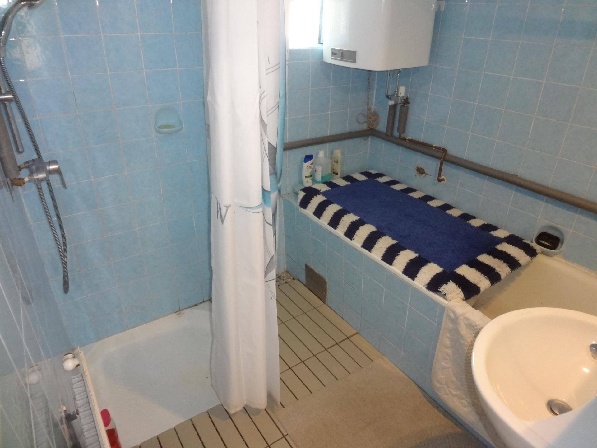 Badezimmer mit blauen Fliesen, Badewanne, Dusche und Waschbecken im 80er-Jahre-Stil.