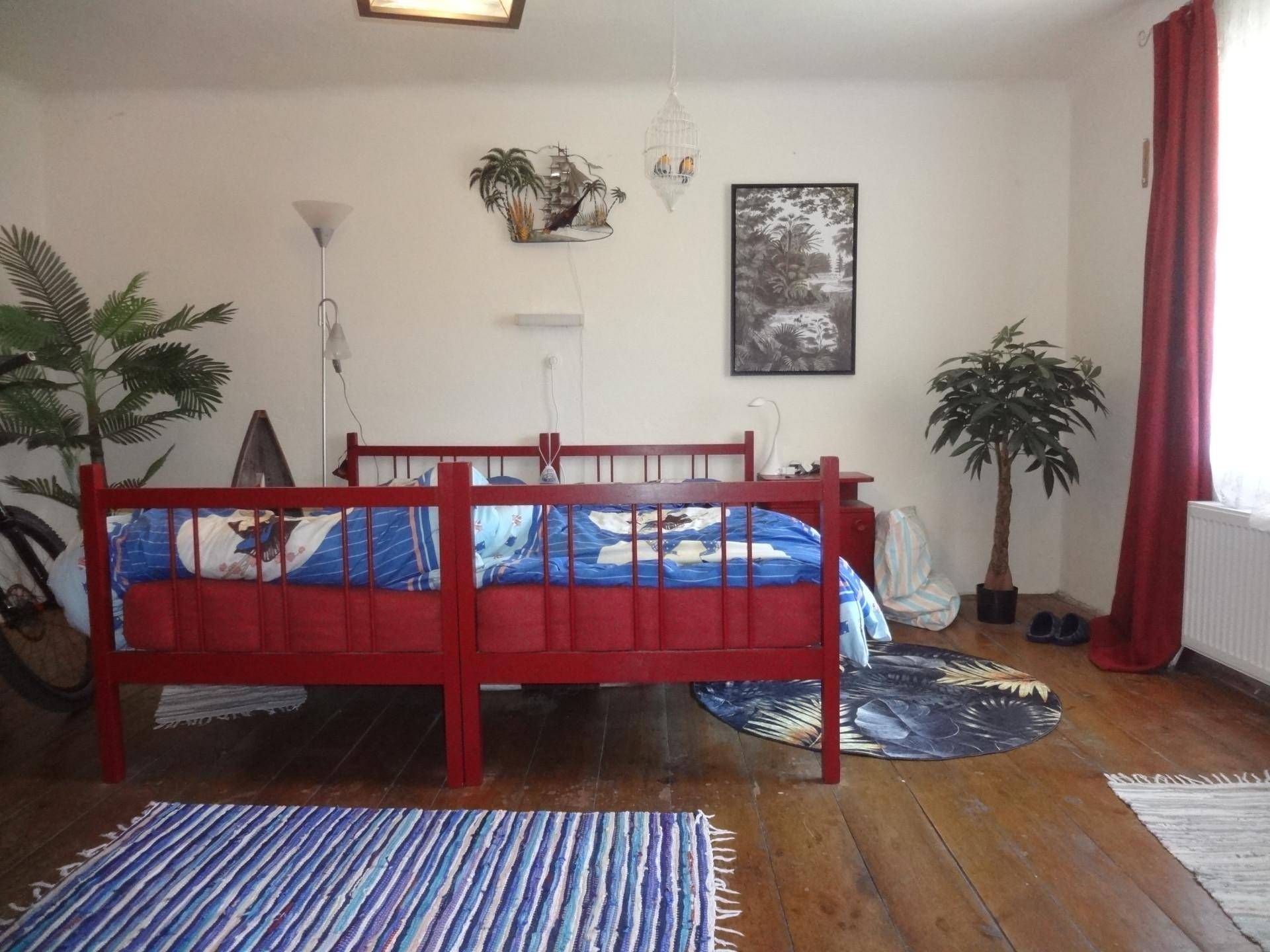Schlafzimmer mit zwei roten Betten, Holzboden und tropischer Dekoration.