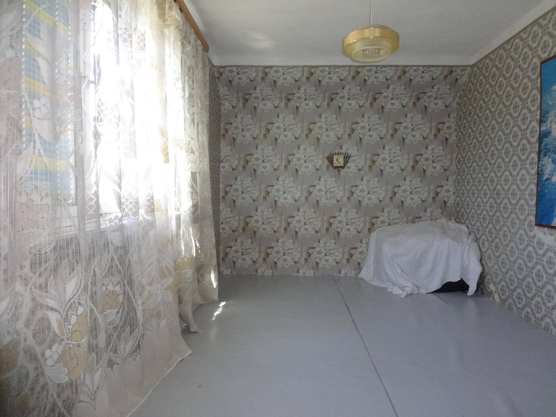 Helles Zimmer mit gemusterter Tapete, großen Fenstern und weißem Boden.