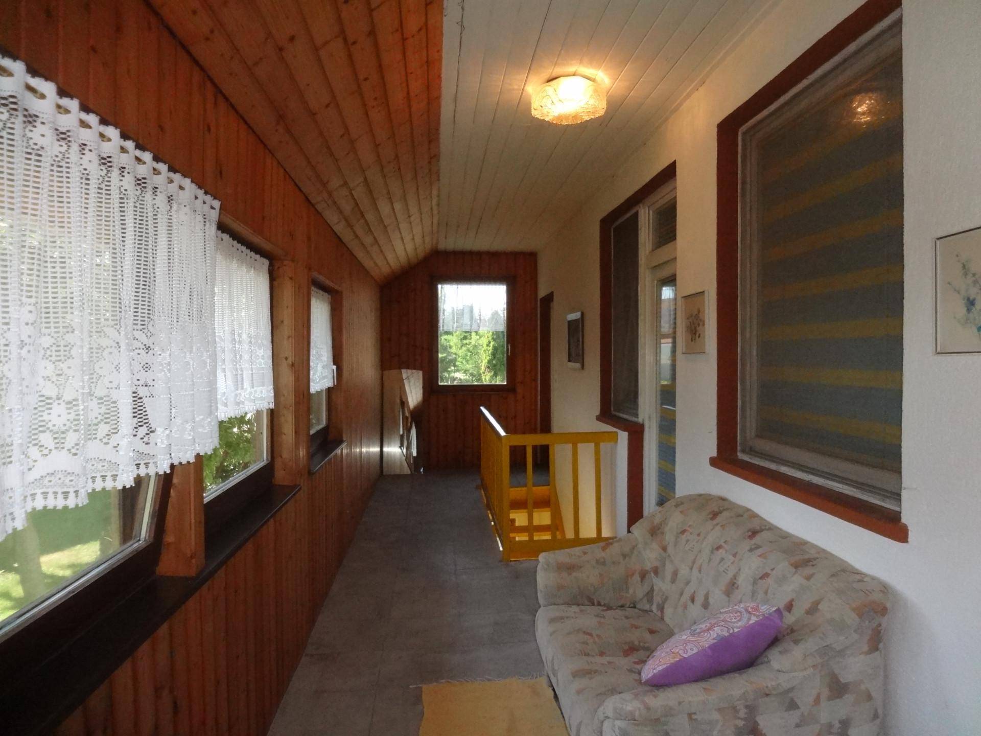 Langer Flur im Obergeschoss mit Holzverkleidung, Sofa und Blick ins Grüne.