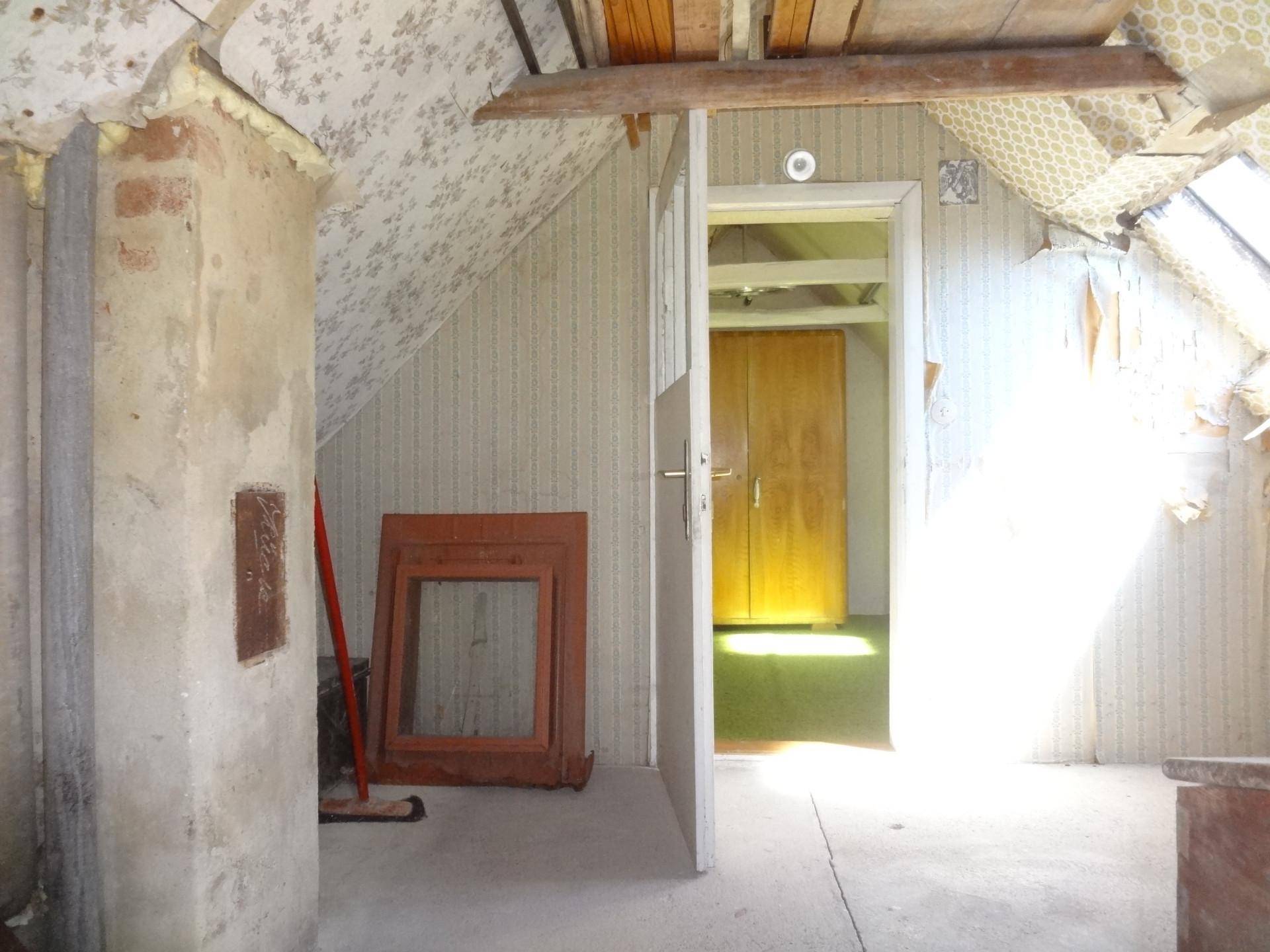 Dachbodenraum mit schrägen Wänden, Holzbalken und Tageslichteinfall, unrenoviert.