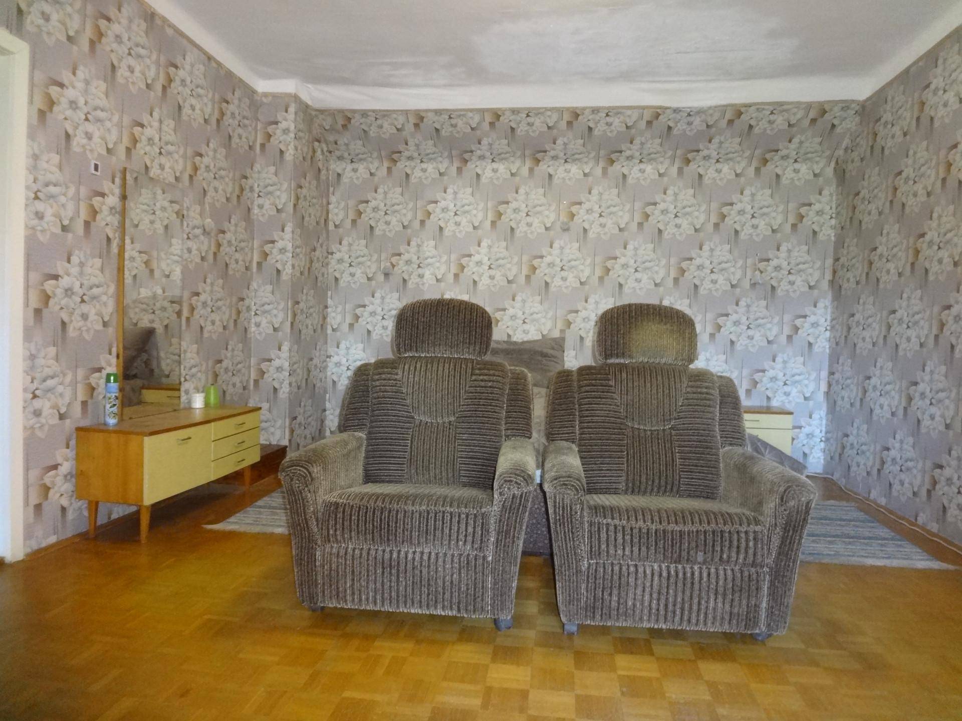Schlafzimmer mit zwei Sesseln, gemusterter Tapete und Parkettboden im Vintage-Stil.