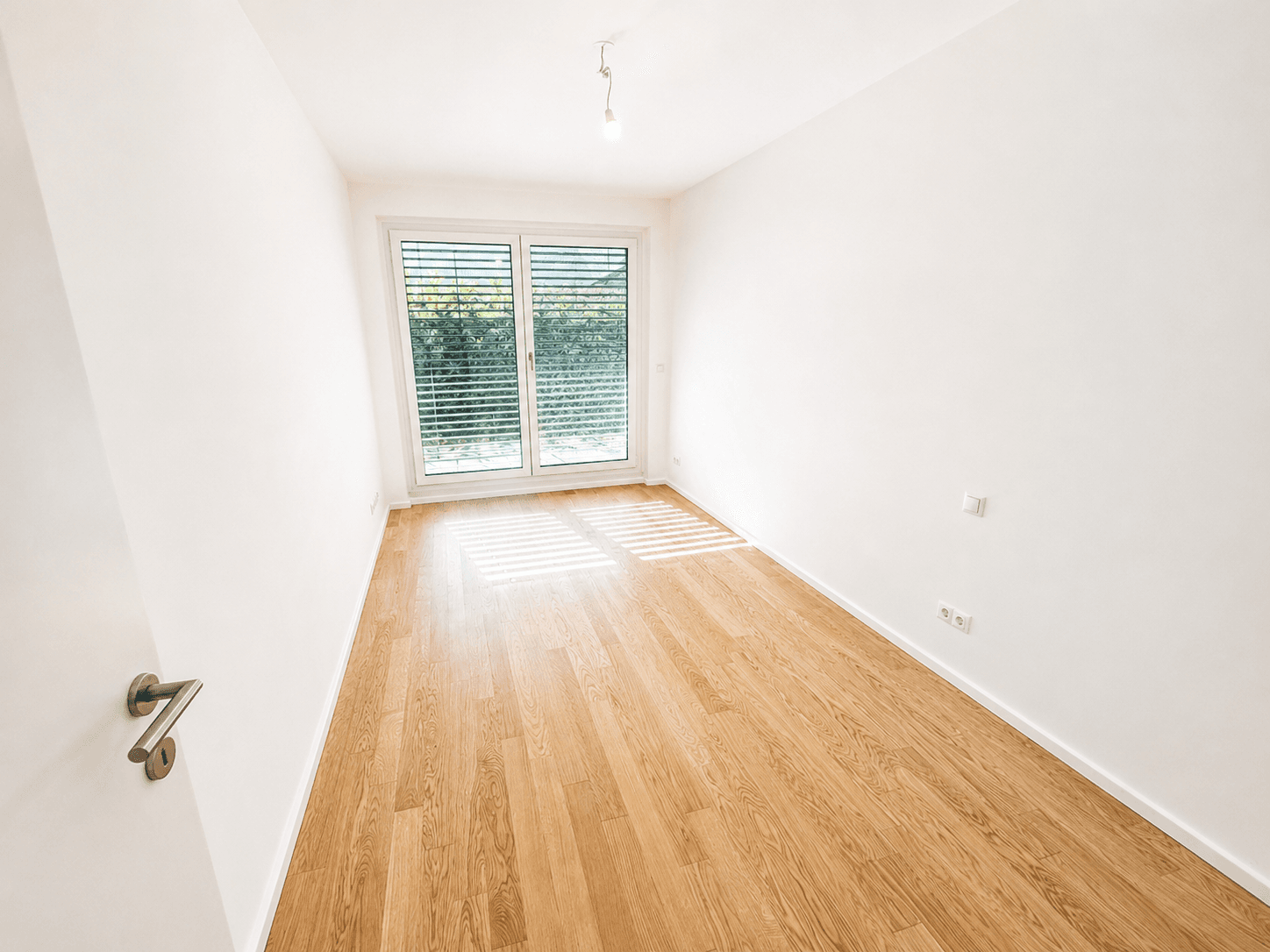 Freundliches Zimmer mit Holzboden und Fenster mit Jalousien für angenehme Lichtverhältnisse.