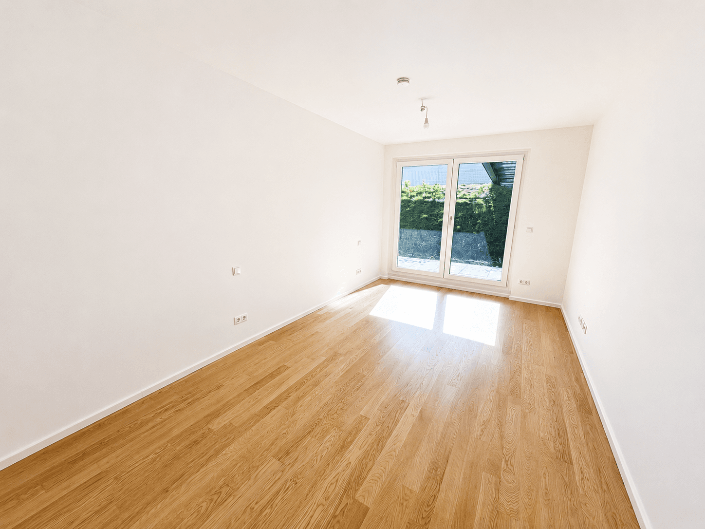 Helles Zimmer mit Parkettboden und Fenster zum begrünten Außenbereich, ideal als Schlafzimmer.