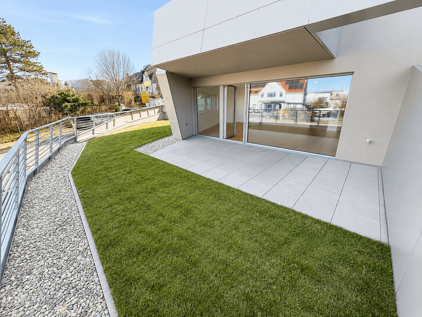Großzügige Terrasse mit Rasenfläche und modernem Gebäudedesign, inklusive barrierefreier Rampe.