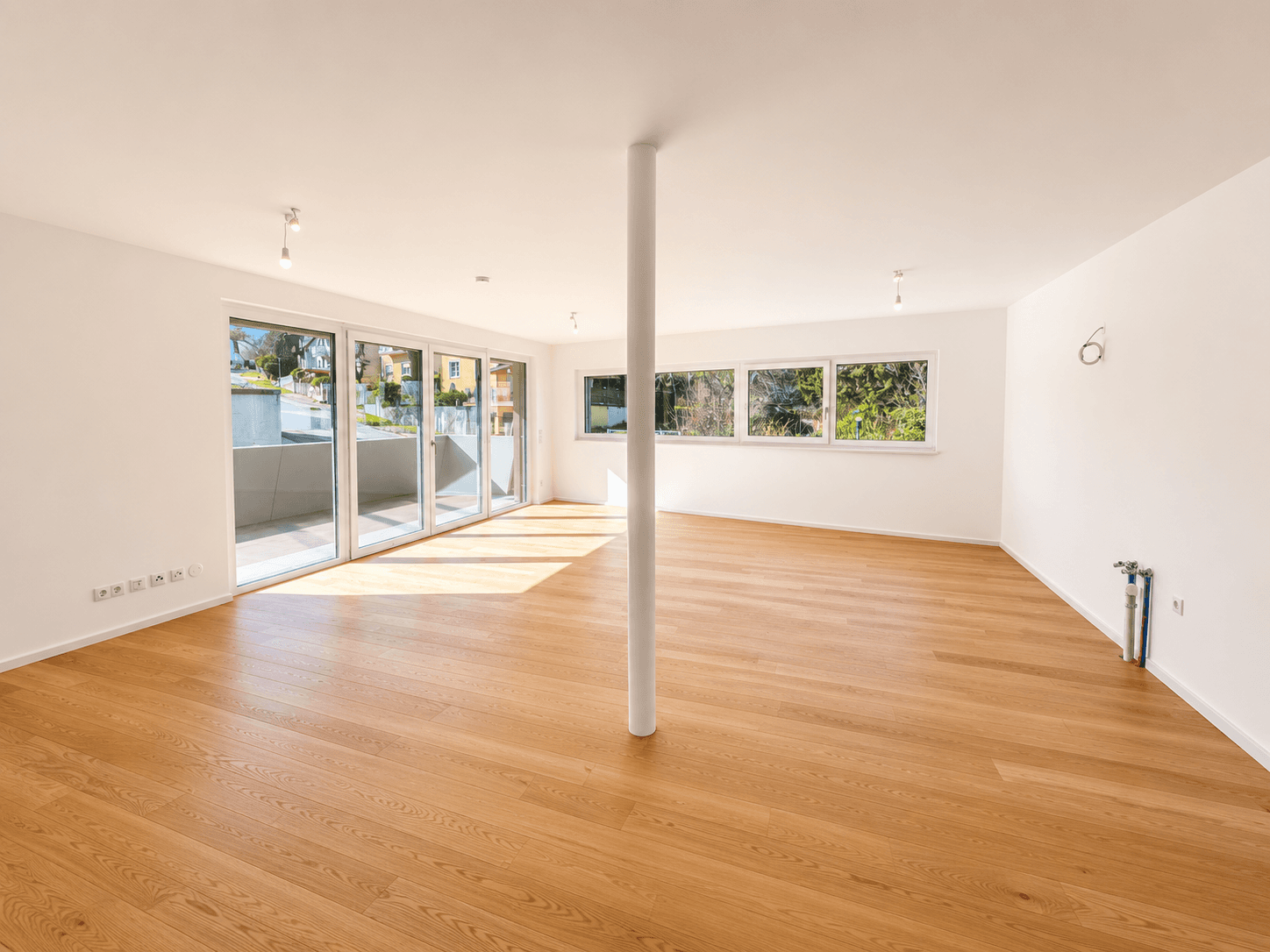 Heller, offener Wohnbereich mit großen Fenstern, Holzboden und viel Tageslicht.