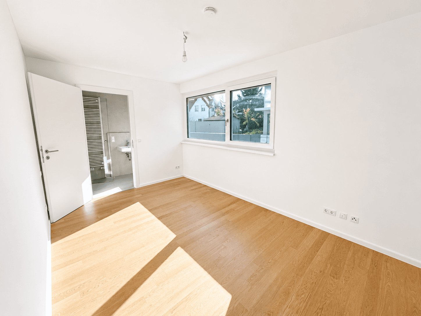 Helles Schlafzimmer mit Holzboden, Fenster und direktem Zugang zu einem modernen Badezimmer.