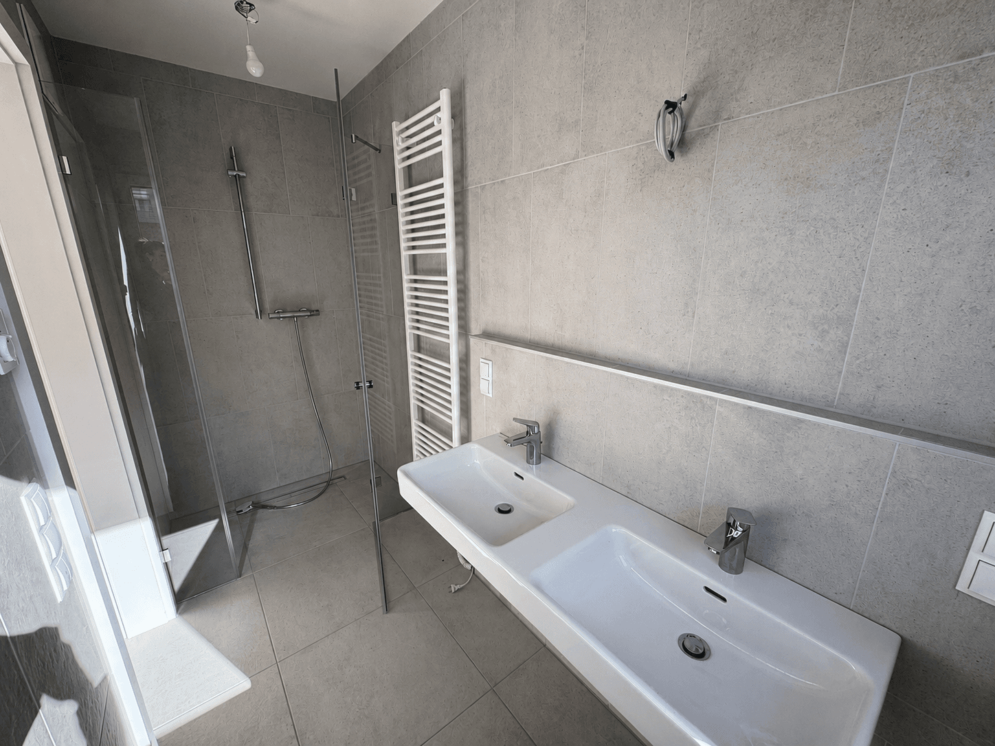 Modernes Badezimmer mit Doppelwaschbecken, begehbarer Dusche und beheiztem Handtuchhalter.