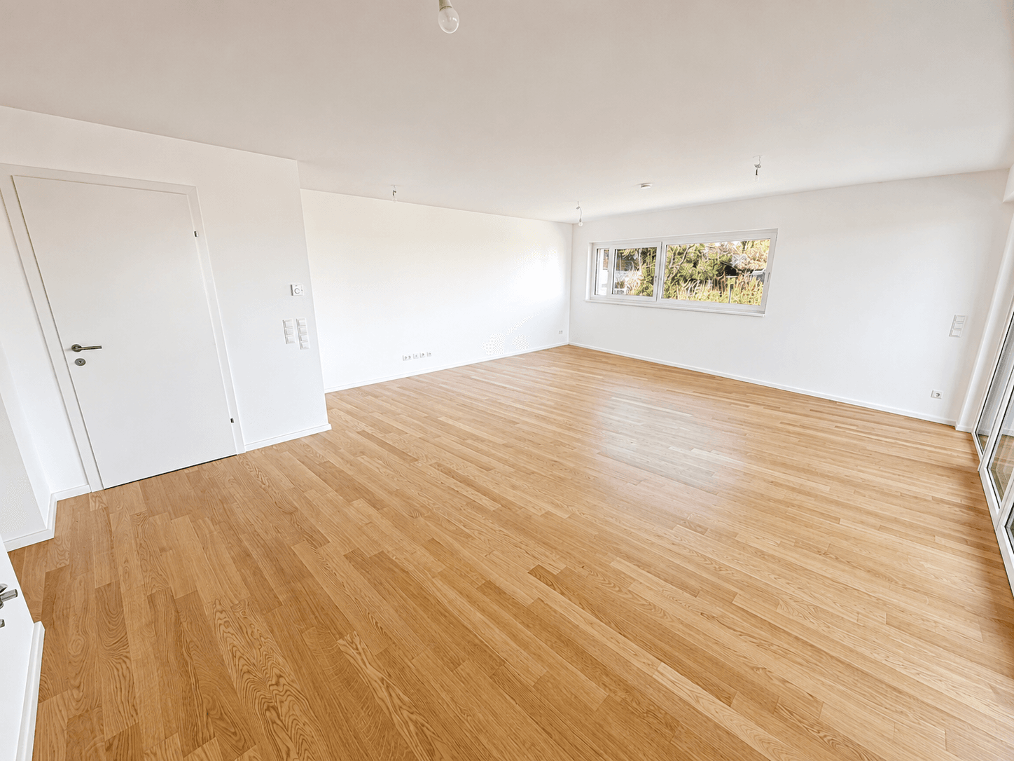 Geräumiges, unmöbliertes Zimmer mit Holzboden und weiß gestrichenen Wänden.