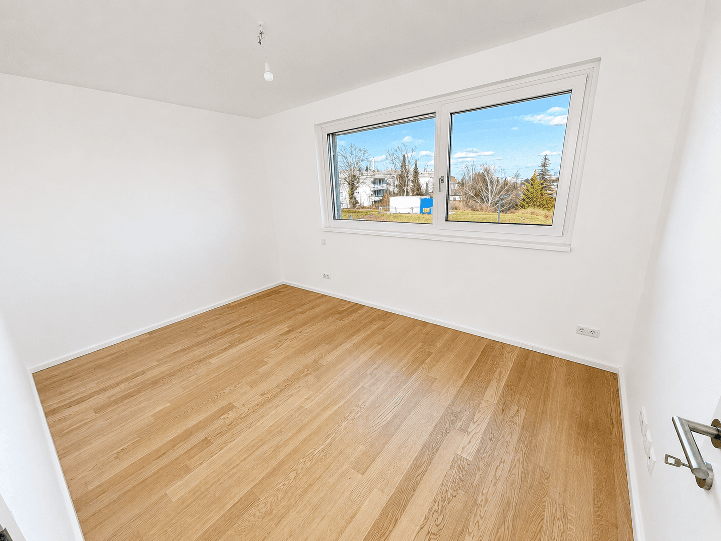 Leeres Schlafzimmer mit Holzboden und einem Fenster mit Blick ins Grüne.