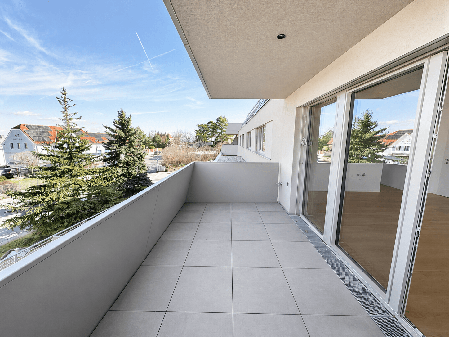 Geräumiger Balkon mit Fliesenboden und Blick auf Bäume und umliegende Häuser.