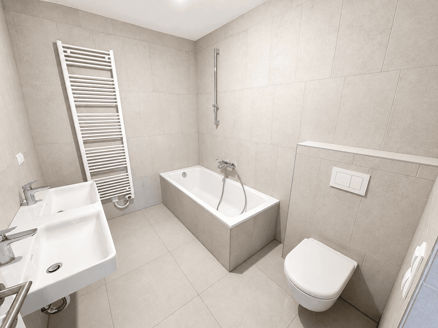 Modernes Badezimmer mit beigefarbenen Fliesen, Badewanne, Doppelwaschbecken und Handtuchheizkörper.