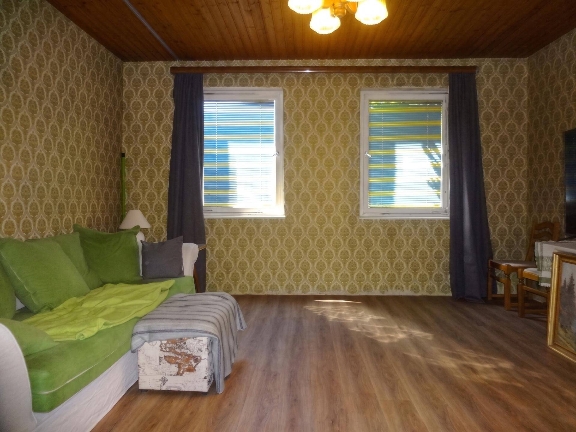 Gemütliches Wohnzimmer mit gemusterter Tapete, Holzbalkendecke und Laminatboden im Vintage-Stil.
