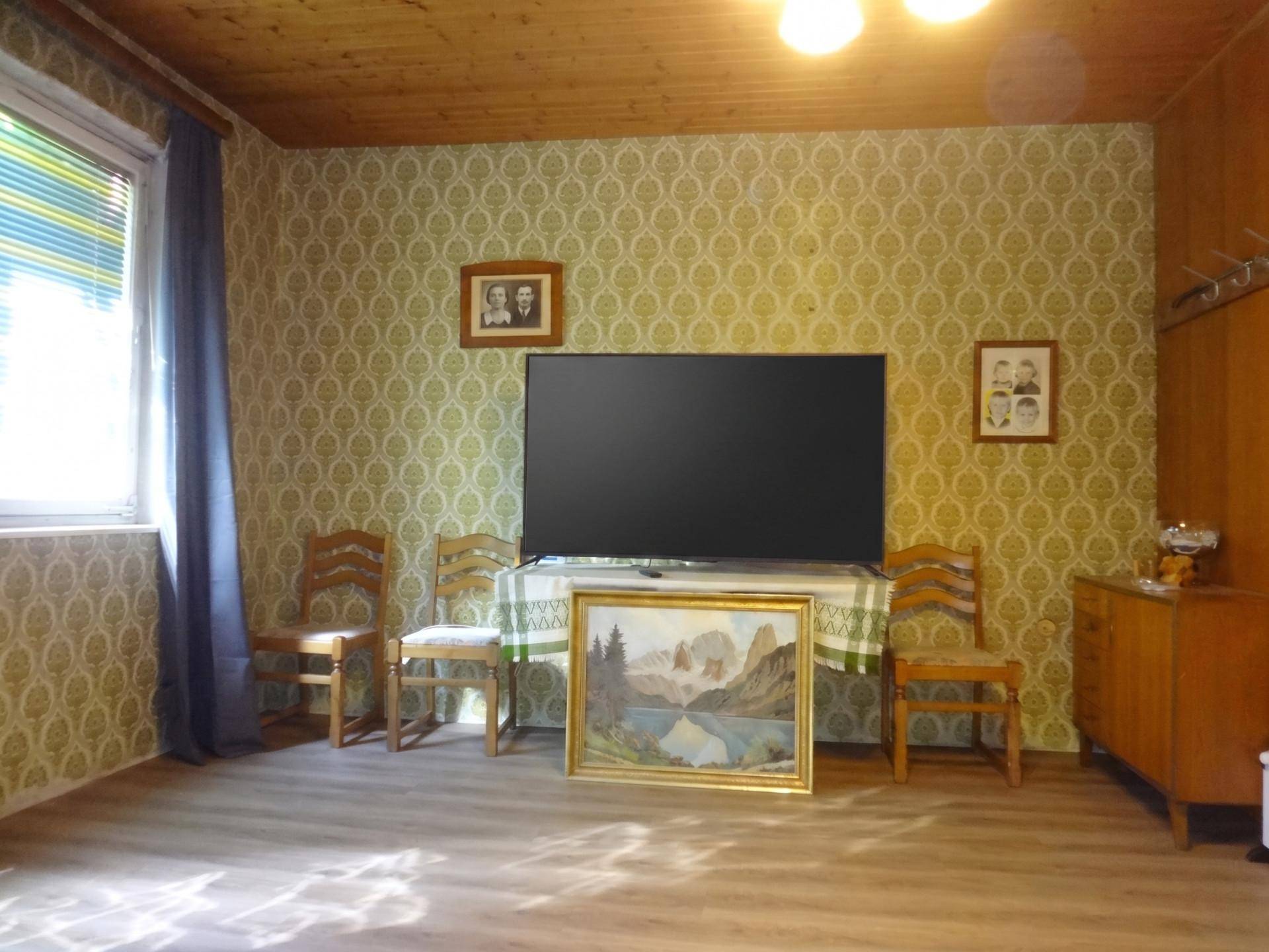 Wohnzimmer mit großem Fernseher, gemusterter Tapete und traditionellen Holzmöbeln.