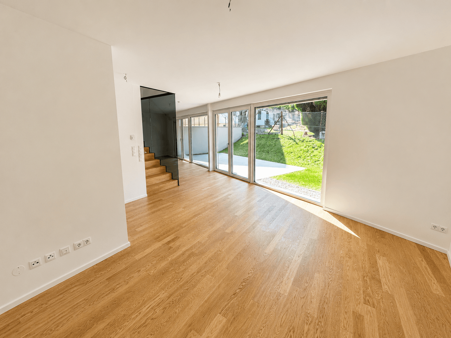 Heller, leerer Wohnbereich mit Eichenparkett, großen Glasfronten und Blick in den Garten.